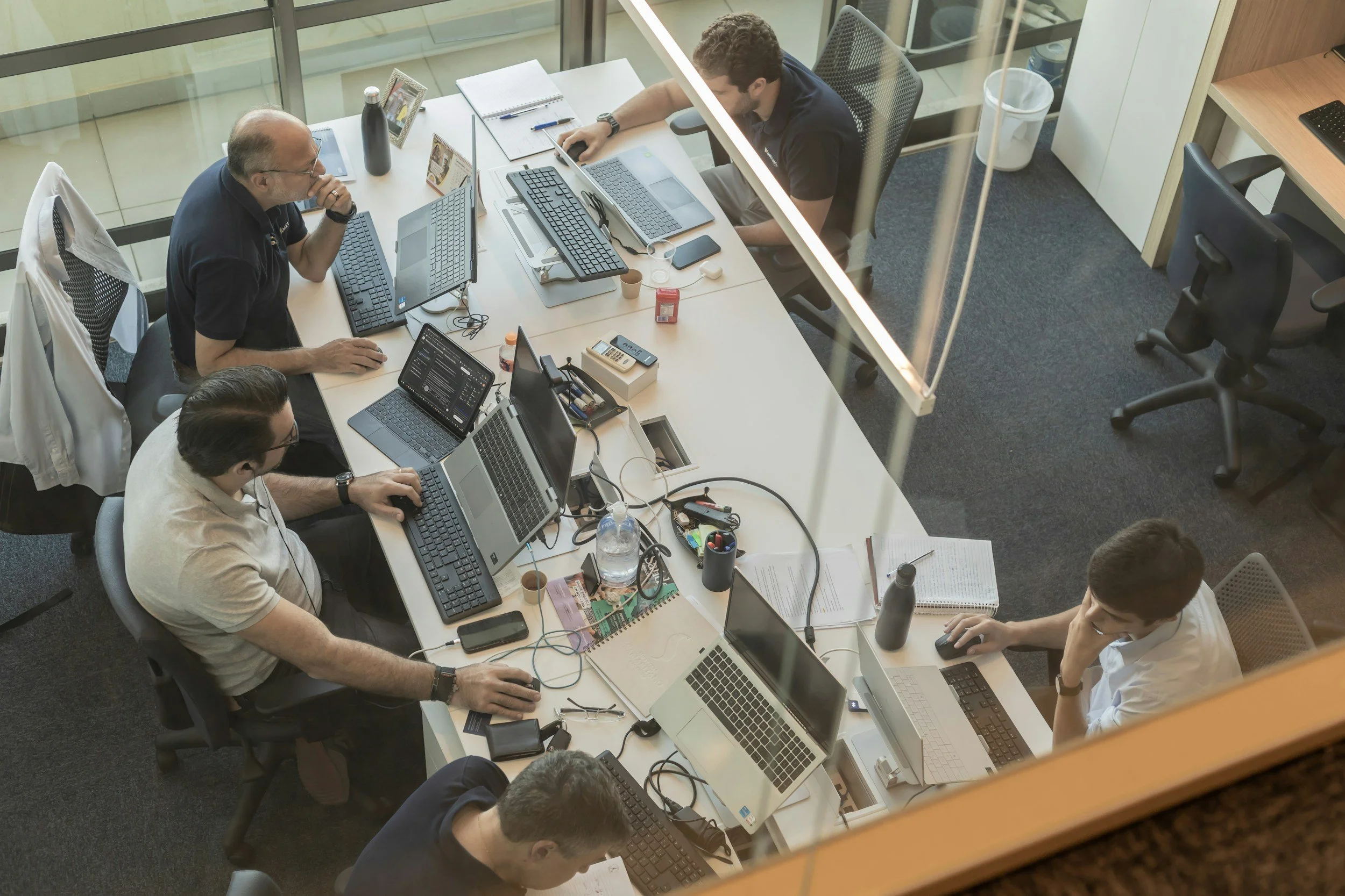 Team von Mitarbeitern sitzen an großem Schreibtisch mit diversen Rechnern