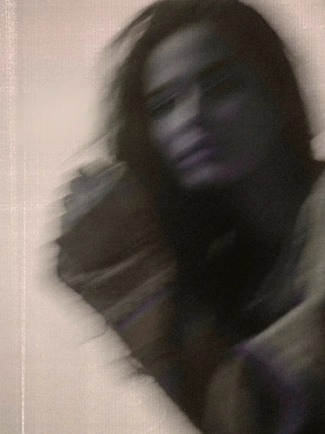 Ein verschwommenes Portrait einer Fraus mit langen Haaren vor einem neutralen Hintergrund.