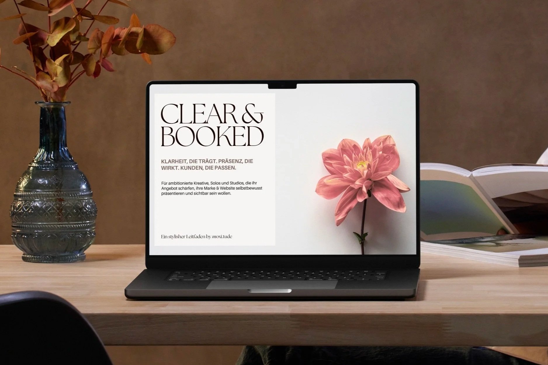 Notebook auf Schreibtisch vor brauner Wand, daneben Vase, Cover von Clear&Booked