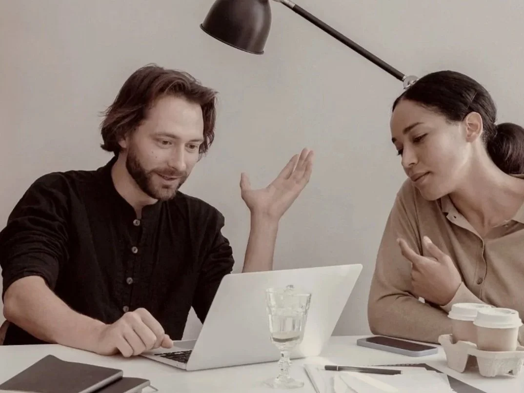 Mann und Frau am Schreibtisch vor Laptop.