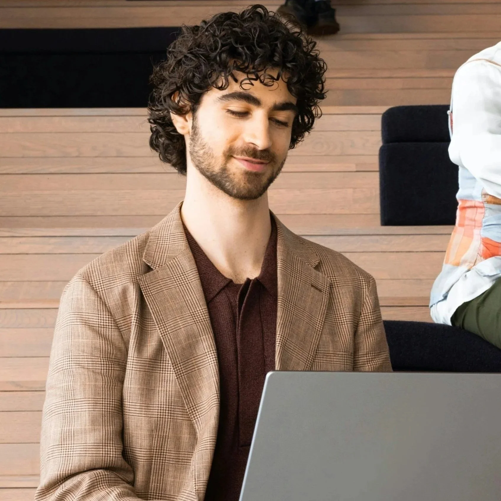Junger Mann mit Bart in hellbraunem Jacket mit Laptop