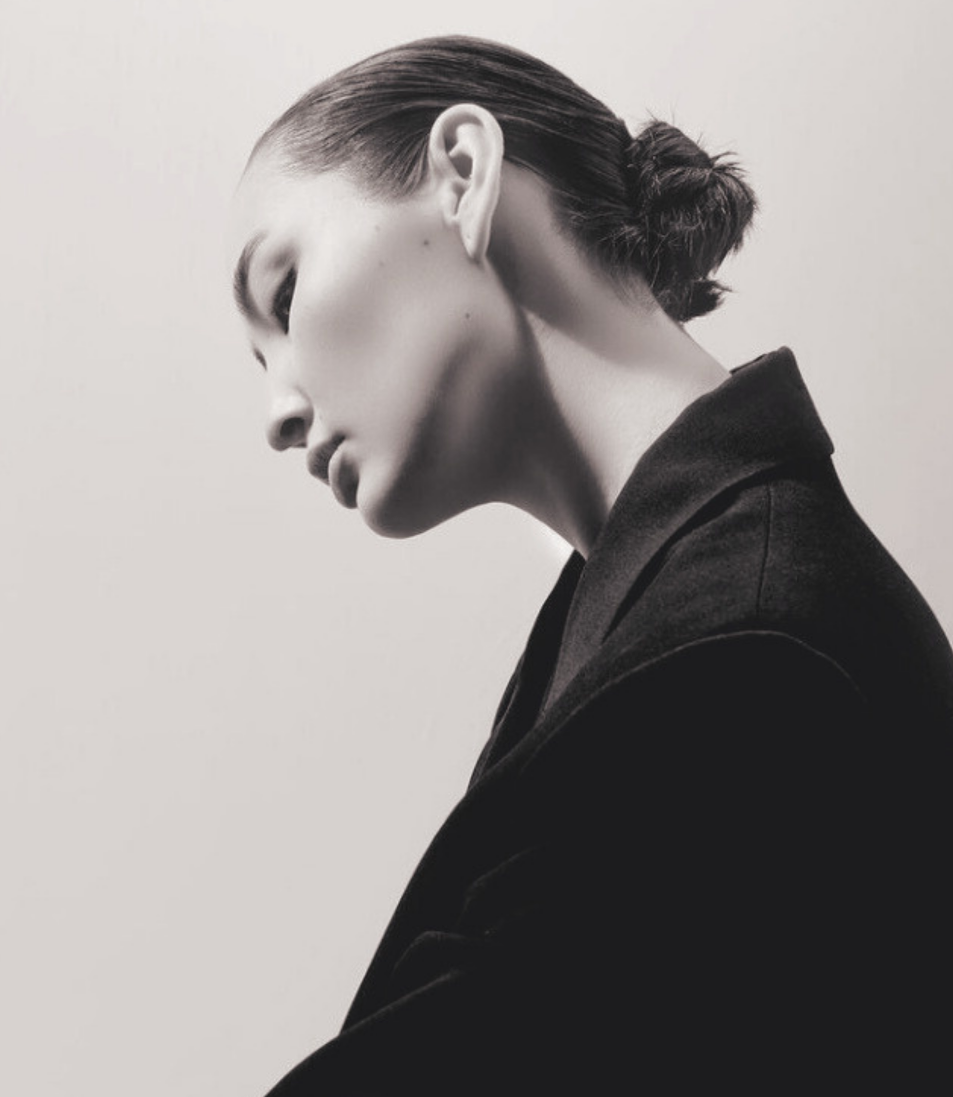 Schwarz-weiß-Fotografie eines jungen Mannes mit seitlich gescheiteltem Haar, zu sehen in Nahaufnahme, mit Blick nach unten und nach links gerichtet.