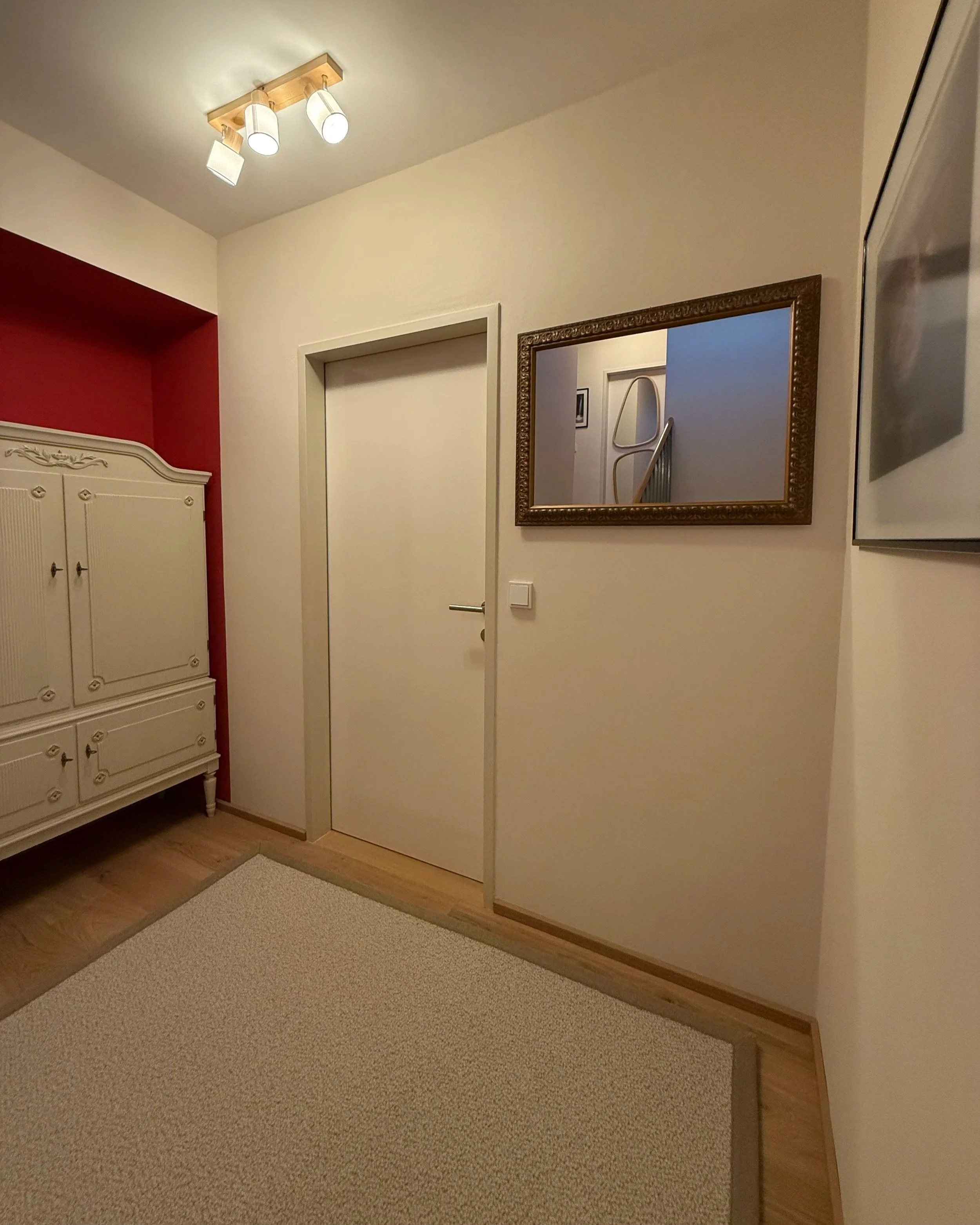 Stiegenhaus im Zwischengeschoss nach der Renovierung. Warme cremefarben, Echtholzparkett, ein Wollteppich und der weiße Schwedische Schrank vor der kirschroten Nische