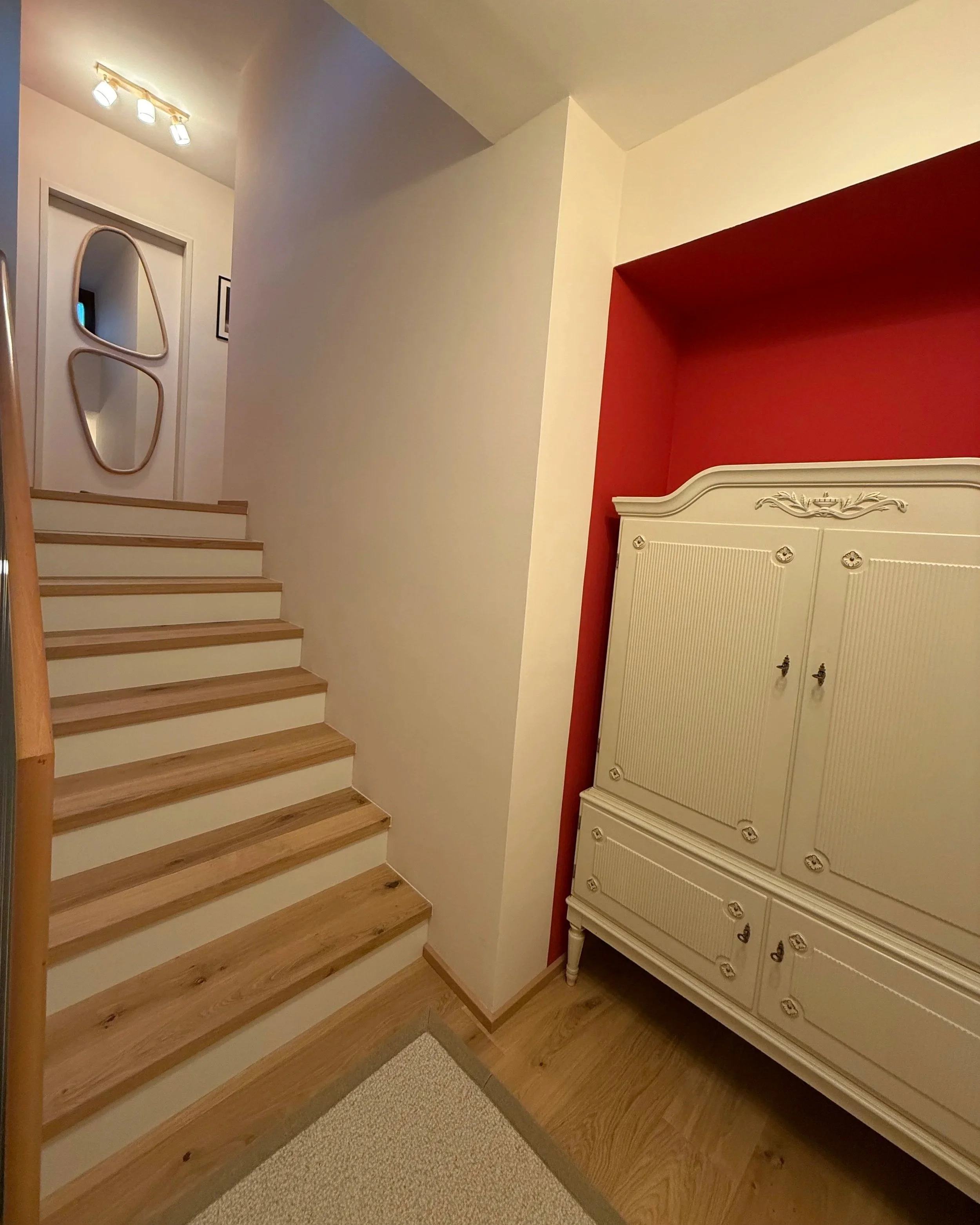 Stiegenhaus im Zwischengeschoss, der weiße Schrank wird durch die kirschrote Wand gerahmt; im Obergeschoss erhält die nun verschlossene Tür dank der Spiegel für den Flur besondere Tiefe
