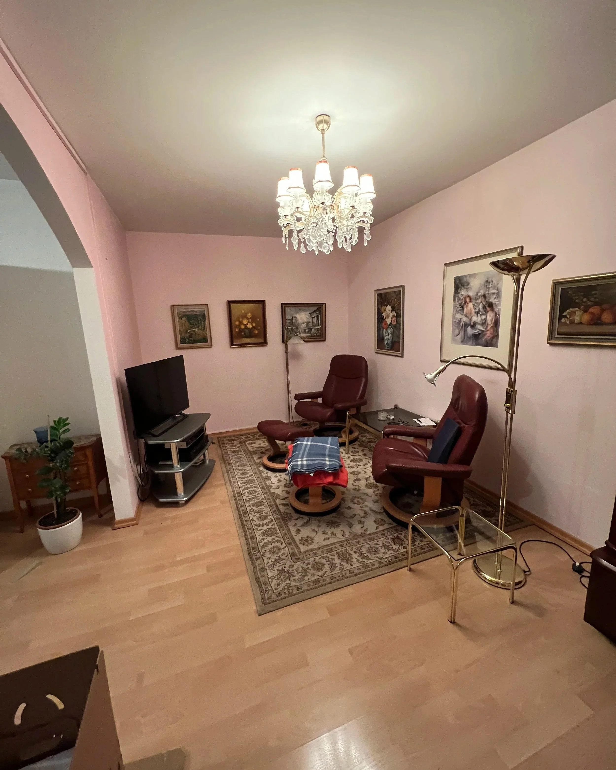 Nebenraum im Zwischengeschoss vor der Renovierung mit Fernseher, zwei Sesseln und rosa Wänden
