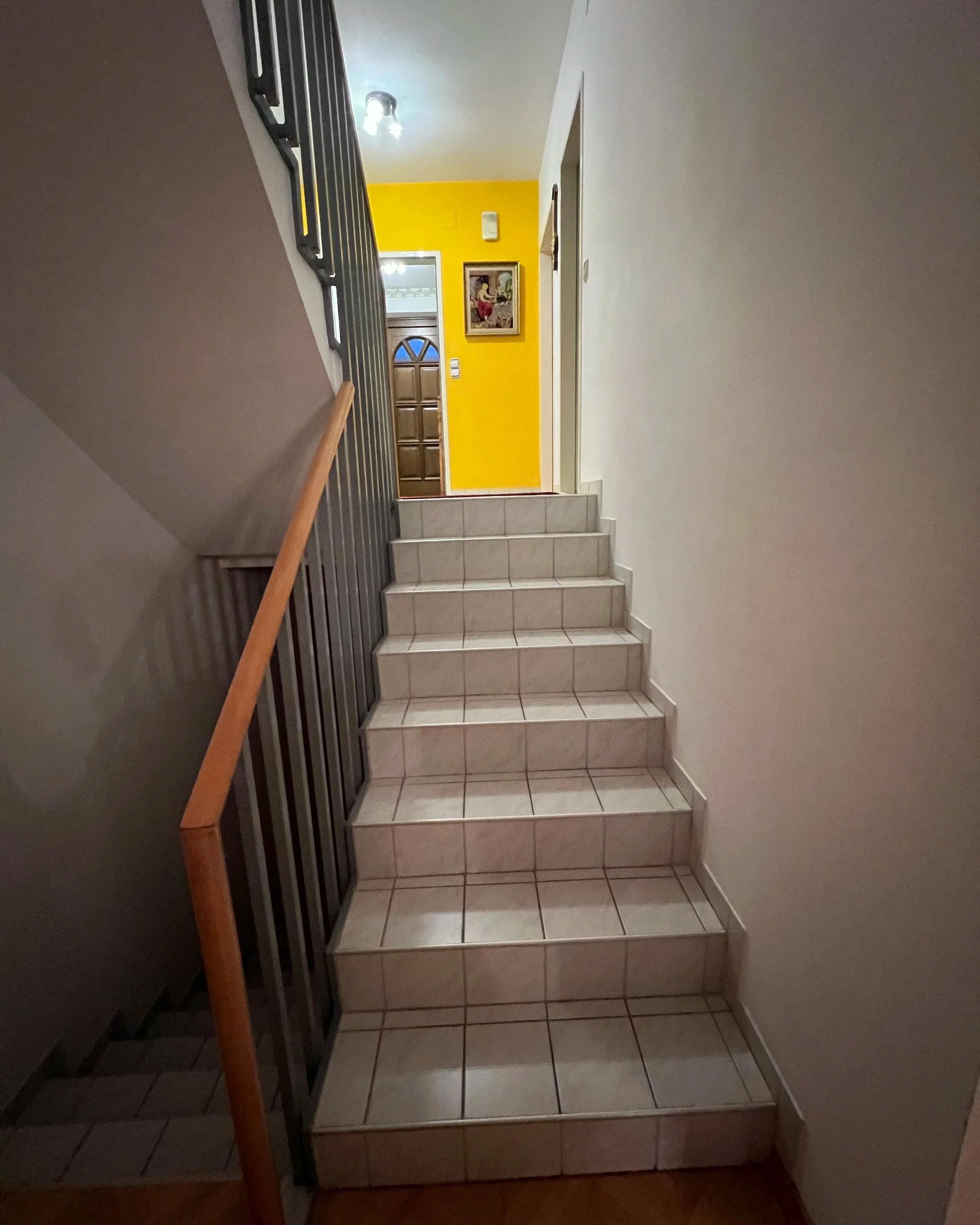 Stiegenaufwang vom Wohnzimmer in EG vor der Renovierung mit weißen Fliesen in Blickrichtung der gelben Wand im Erdegeschoss
