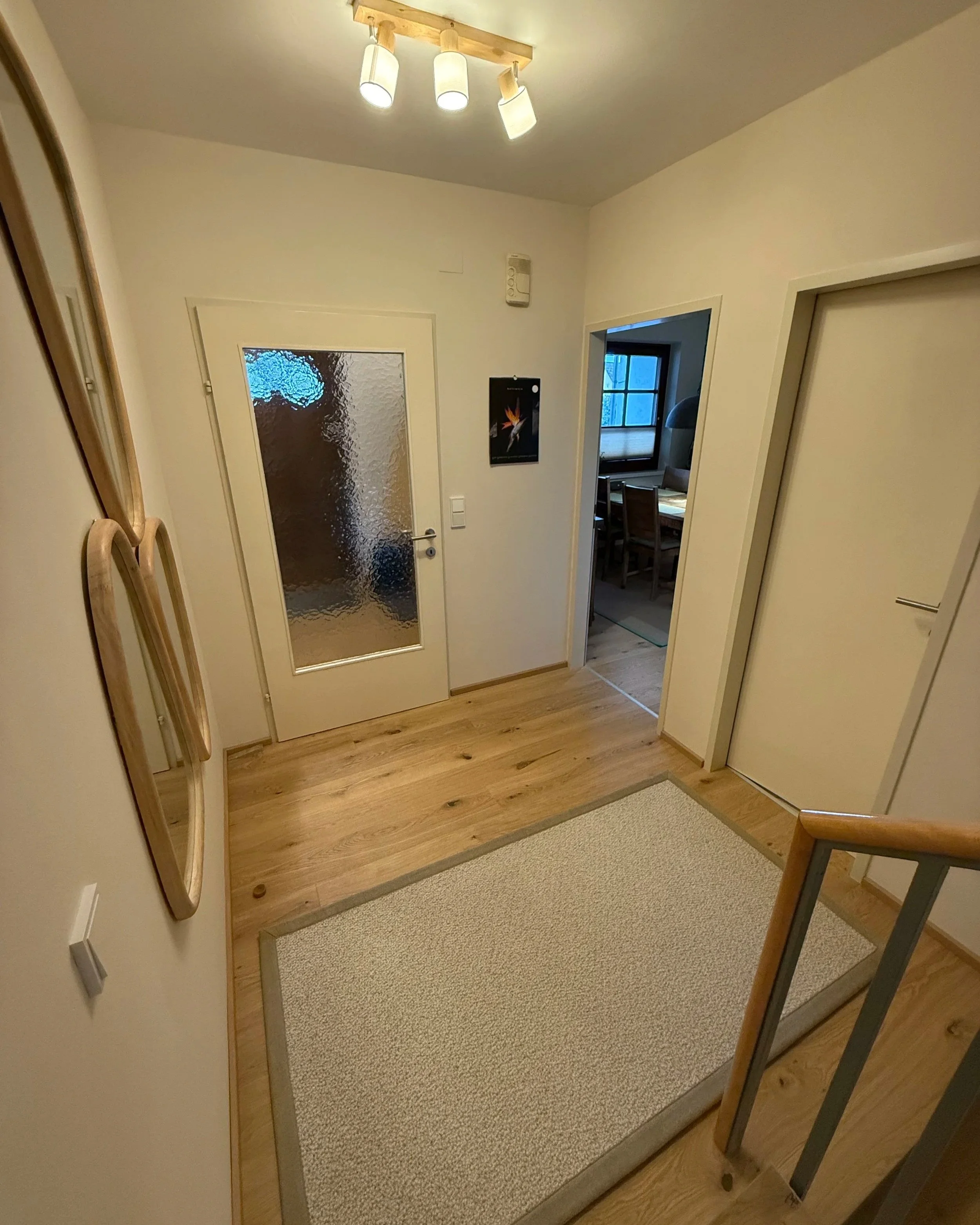 Stiegenhaus im Erdgeschoss, warmer Eichenparkett mit Wollteppich vor den Stufen und Spiegel in organischer Form mit Echtholzrahmen