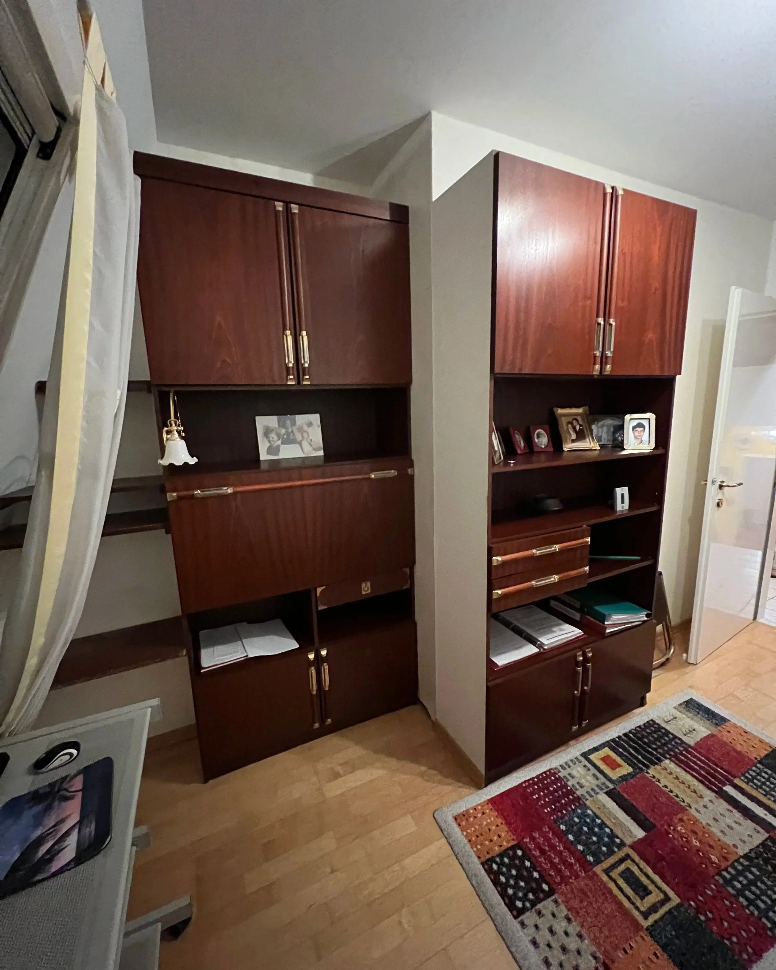 Nebenraum im OG vor der Renovierung. Ein schmaler Raum mit hohen Schränken, Schreibtisch und einem bunten Teppich