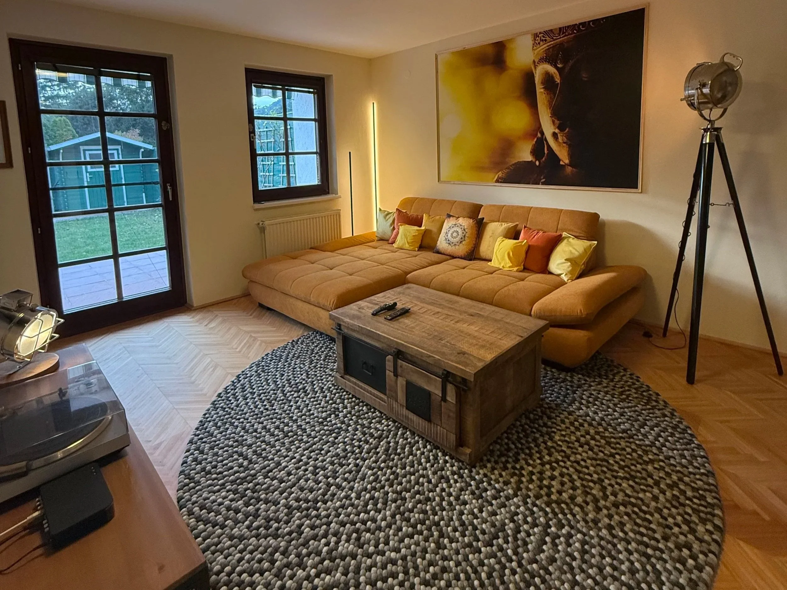 Warme Töne, eine großzügige Sofalandschaft, das gerahmte Wandbild und der graue Filzkugelteppich bilden eine  wohlige Einheit