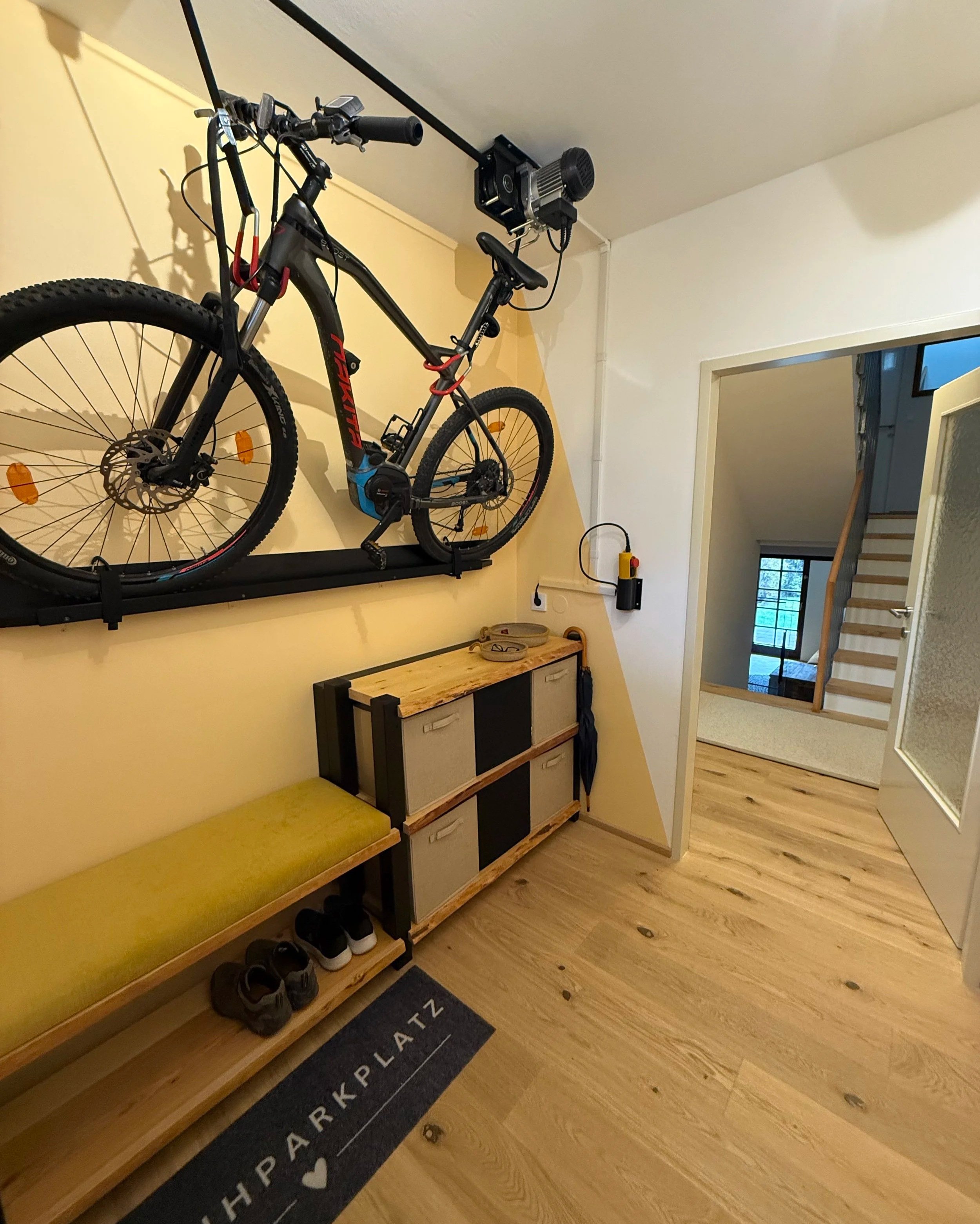 Windfang / Flur nach der Renovierung. Mit angefertigter Bank-Regalkombination aus Vollholz, einem weichen goldgelben Polster und Stoffkisten für Stauraum.