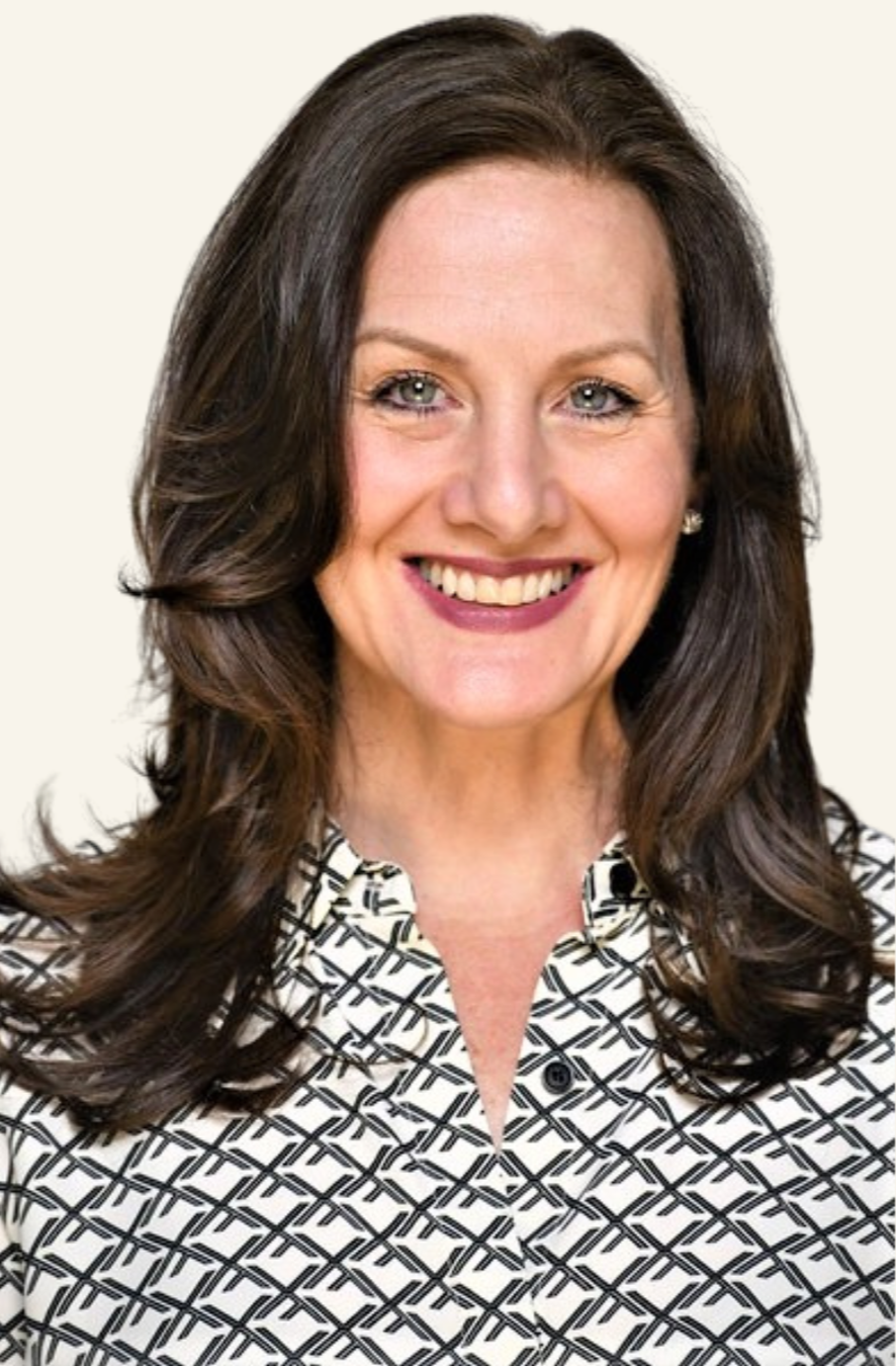 A woman with long dark brown hair, blue eyes, and wearing a patterned blouse, smiling at the camera.