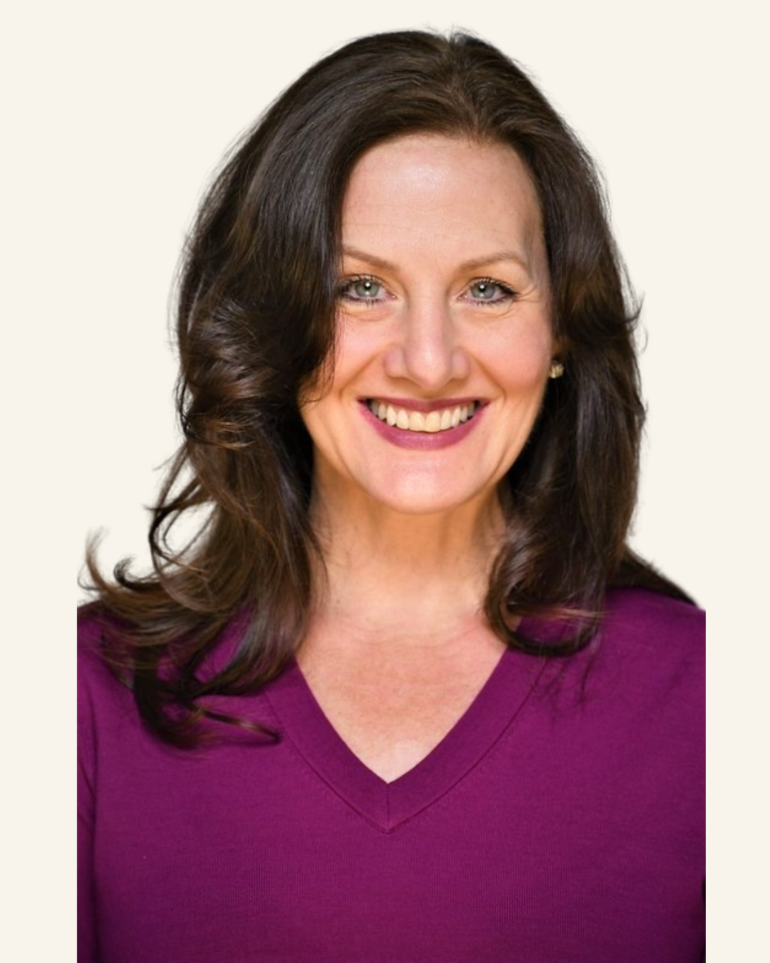 A woman with dark brown, wavy hair smiling, wearing a purple V-neck shirt, positioned against a plain white background.
