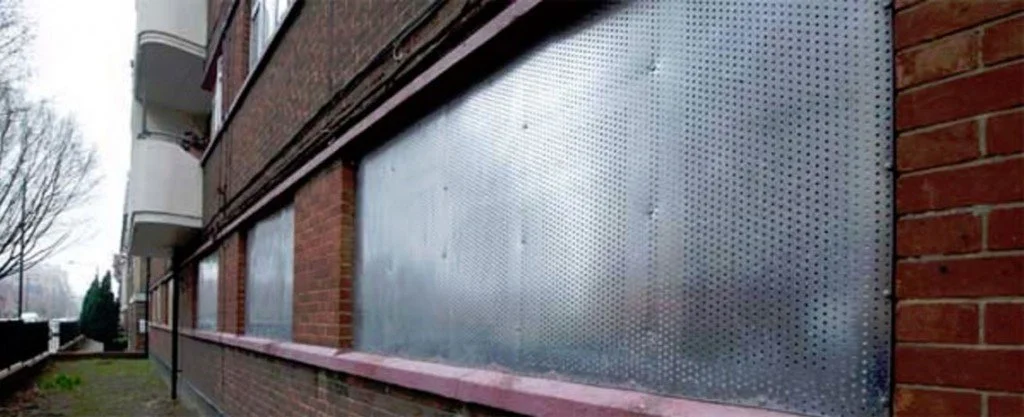 Metal panels with perforated holes installed on the exterior of a brick building.