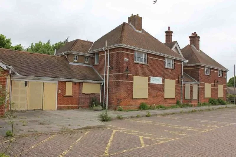 Abandoned brick building with boarded-up windows in a parking lot.