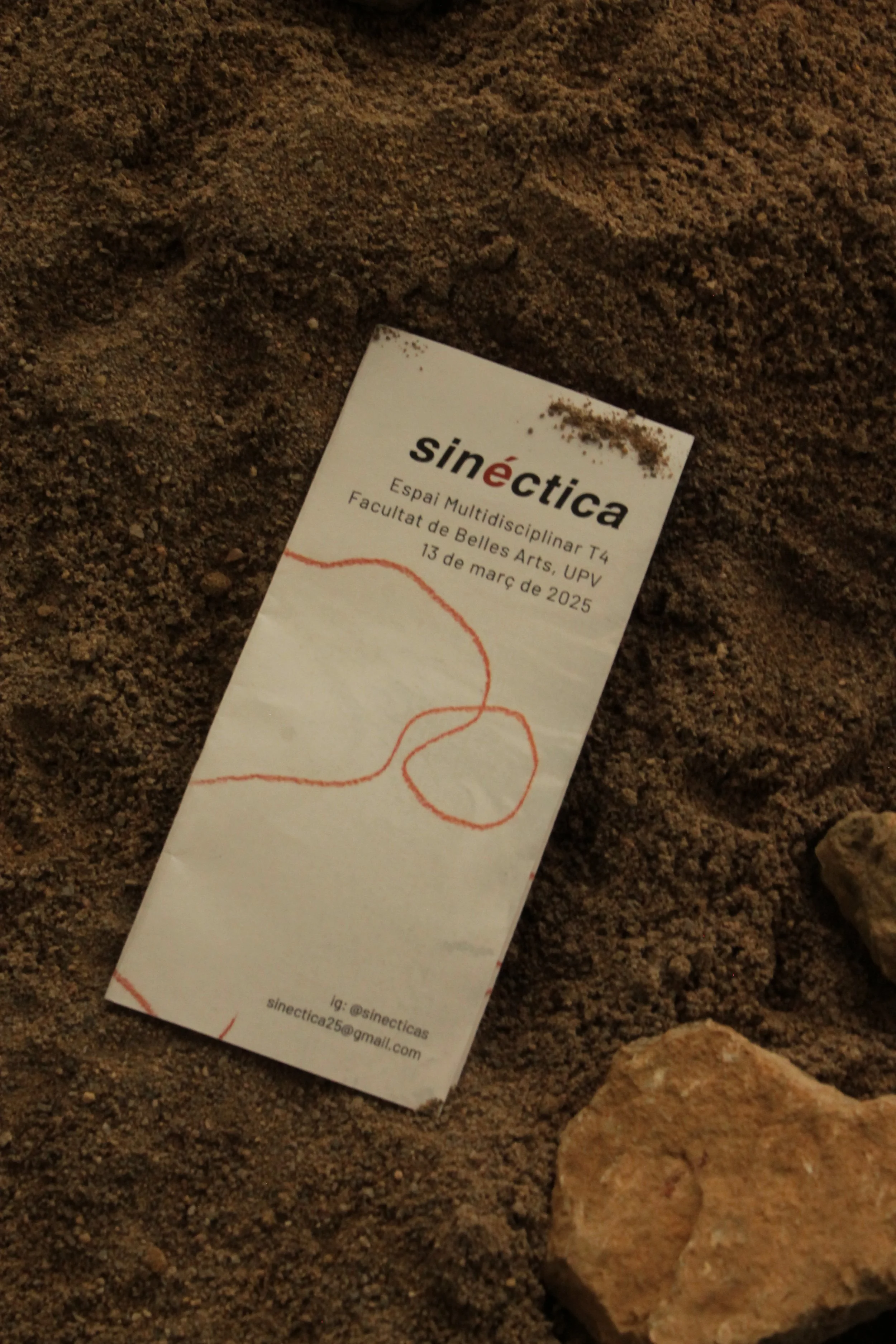 Una tarjeta de invitación puesta sobre arena, con el texto 'sine|ctica', invitando a un evento en la Facultad de Bellas Artes, UPV, el 13 de marzo de 2025, y con una ilustración de una línea roja curvada.