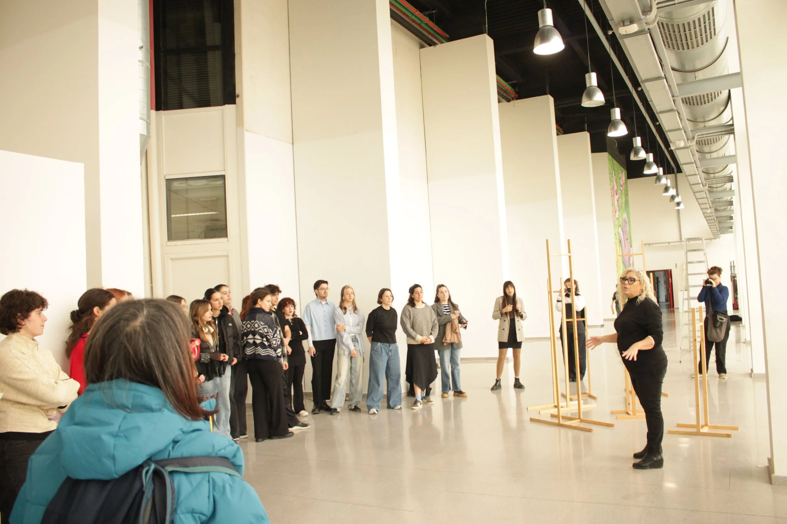 Grupo de personas en una visita guiada en un espacio interior, escuchando a una guía que explica algo, con algunas personas tomando fotos.