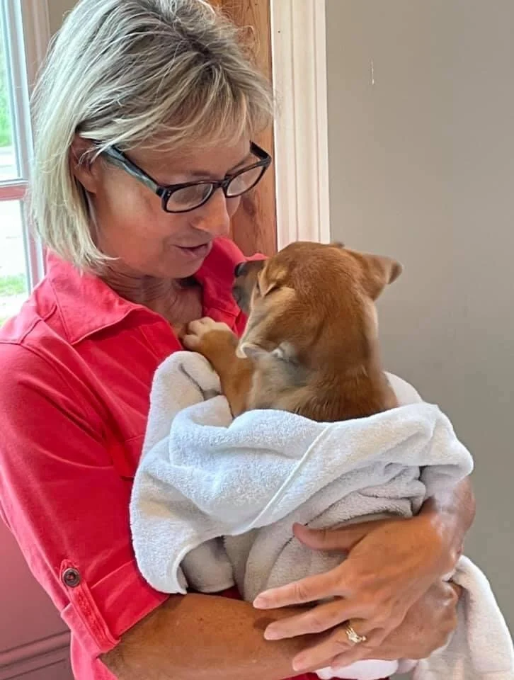 A woman holding a small brown dog wrapped in a white towel, with both faces close together, inside CASA Clinic.