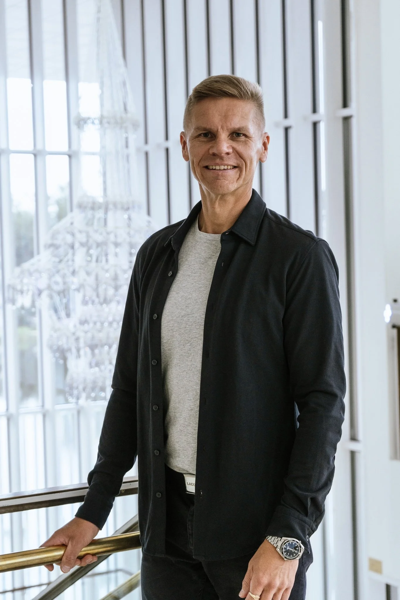 Kuva miehestä seisomassa hotellin aulassa, taustalla suuri kristallikruunu ja suuret ikkunat.