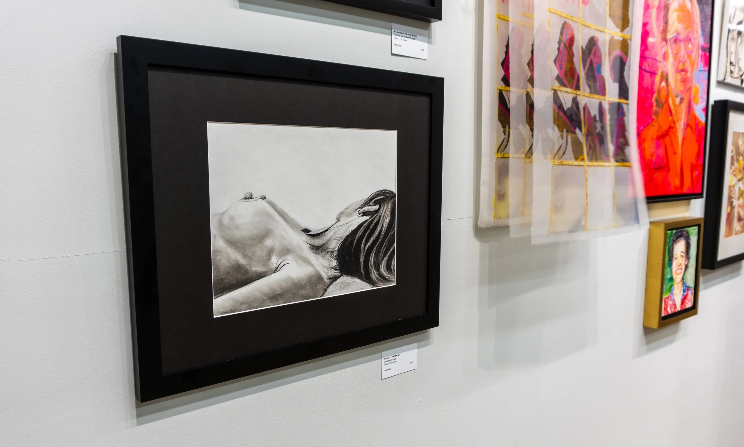 Art gallery wall featuring various framed artworks including a black and white sketch of a woman with long hair resting on a surface, and other colorful portraits and abstract pieces.