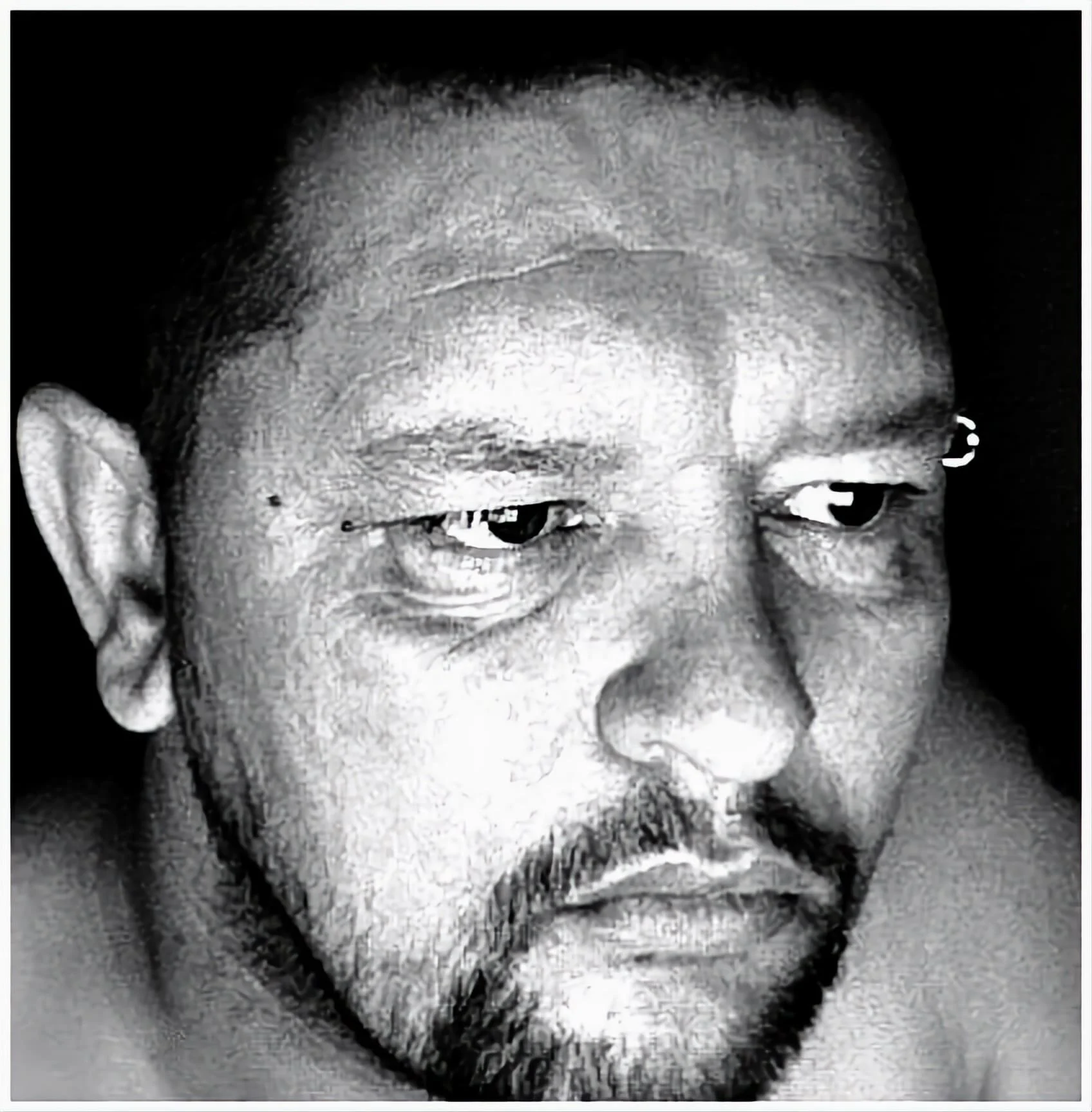 Close-up black-and-white portrait of a man with short hair, a beard, and a mustache, with a serious expression and his eyes looking to the side.