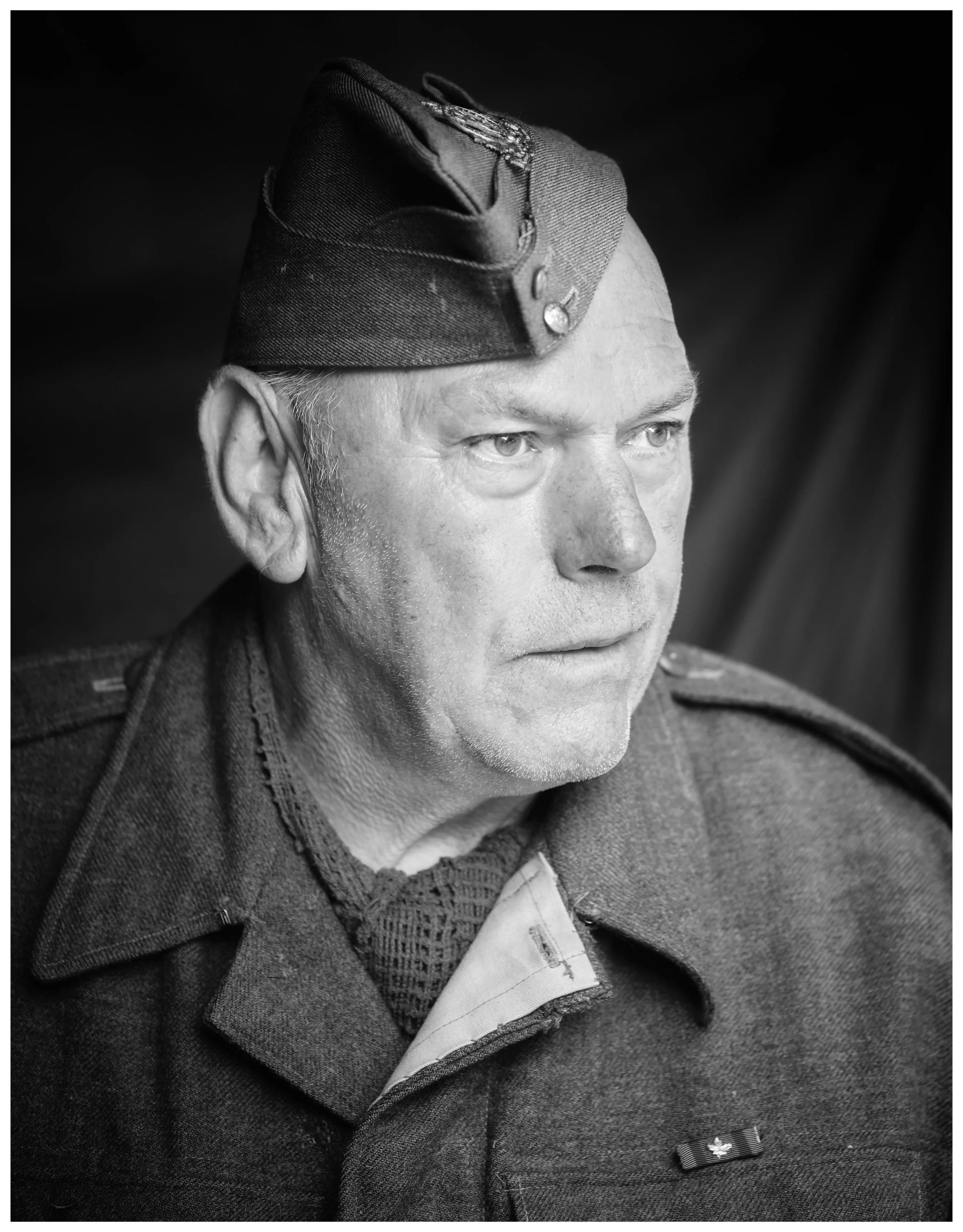 Black and white portrait of an older man in a military uniform, wearing a hat with insignia, looking to the right with a serious expression.