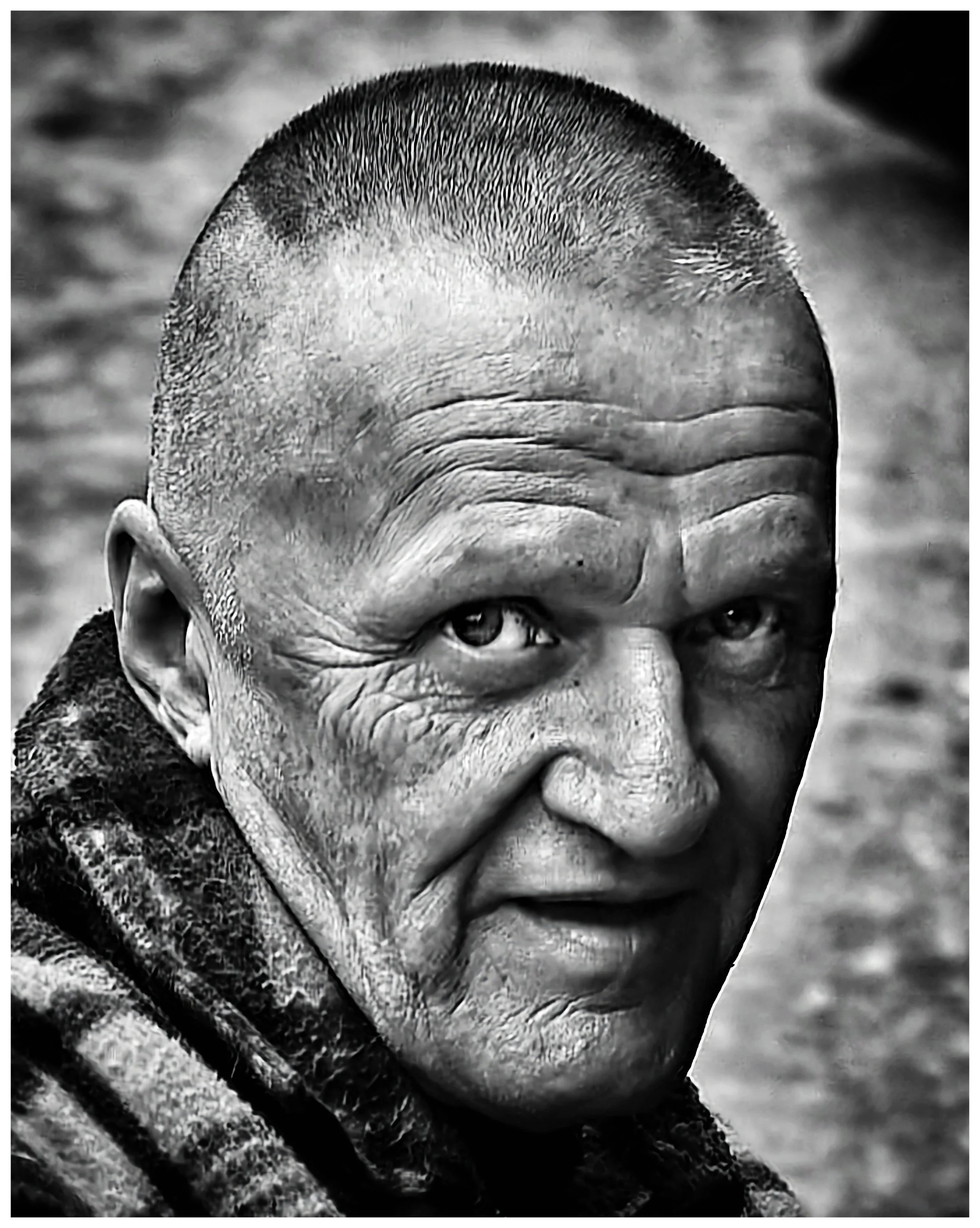 Close-up black and white photo of elderly man with short hair and deep facial wrinkles, looking over his shoulder at the camera.