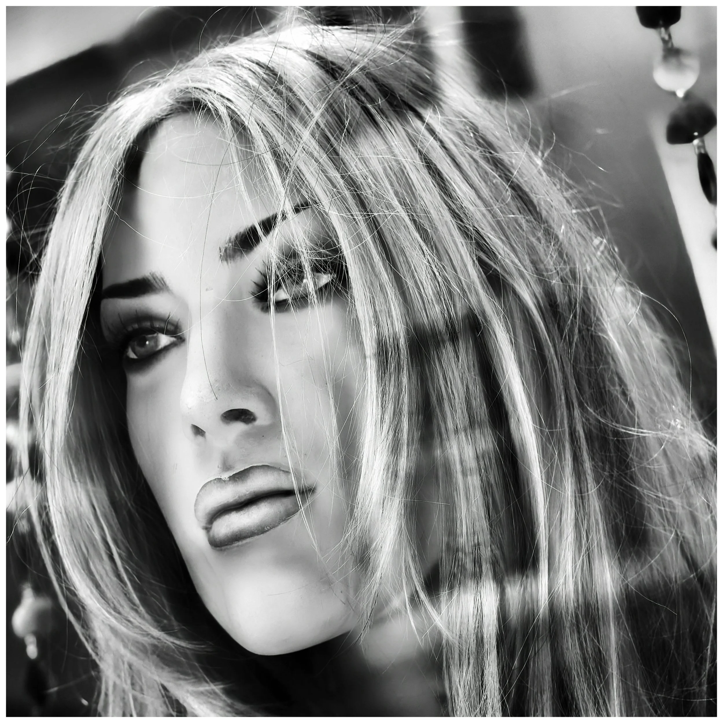 Close-up of a mannequin's face with messy hair, dark eye makeup, and slightly parted lips, in black and white.