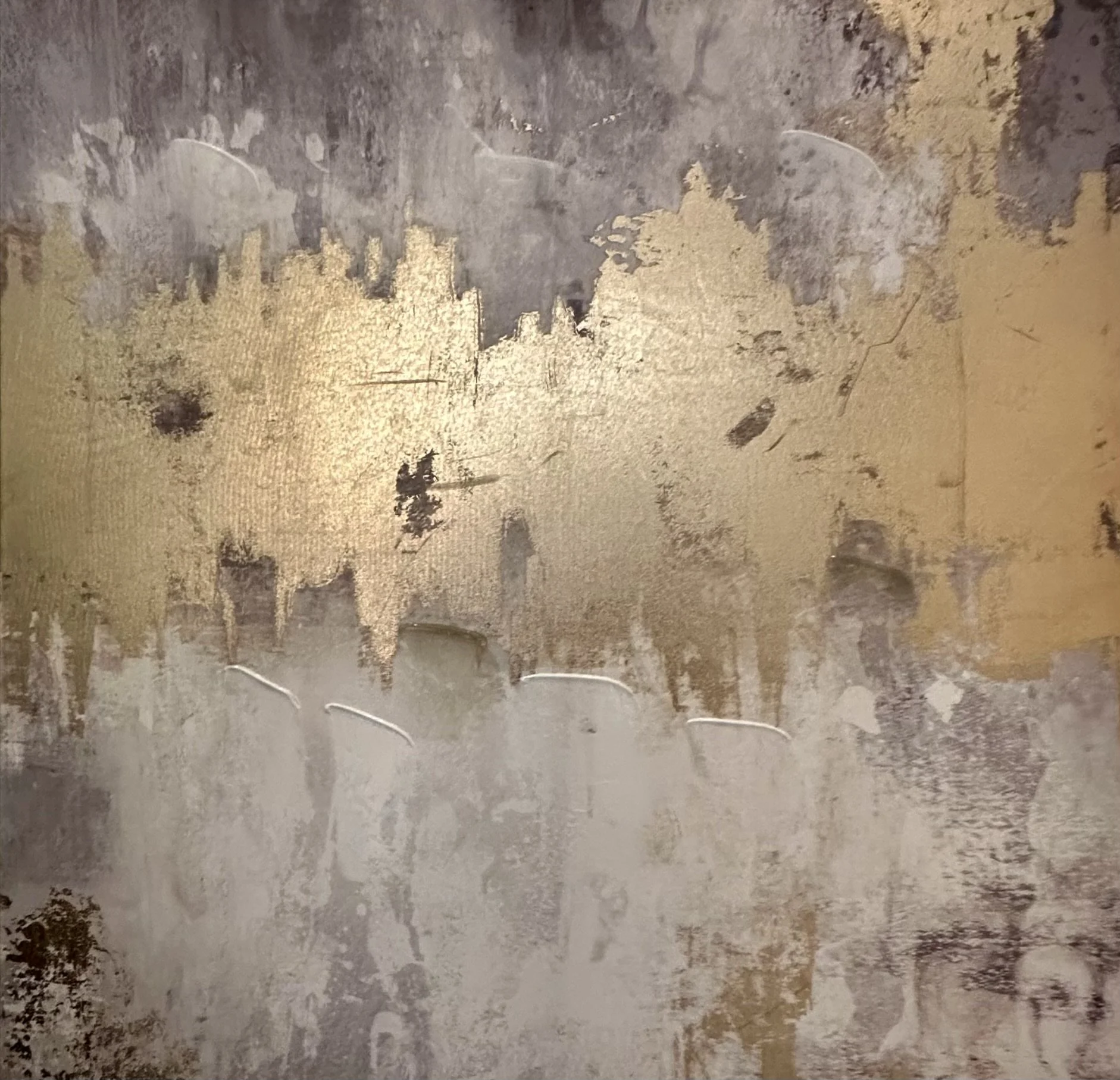 Close-up of a wall with peeling paint and exposed layers, showing a mix of gold, gray, and beige colors.