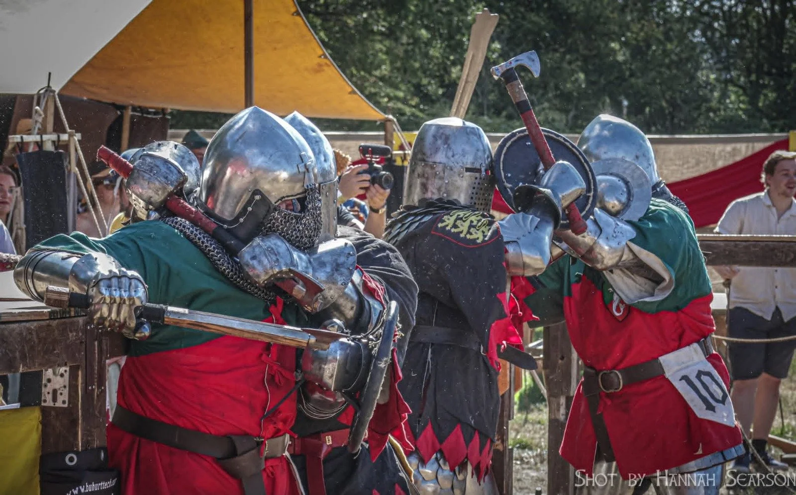 Two knights in shiny armor and colorful tunics engage in combat with swords and shields during a medieval reenactment.