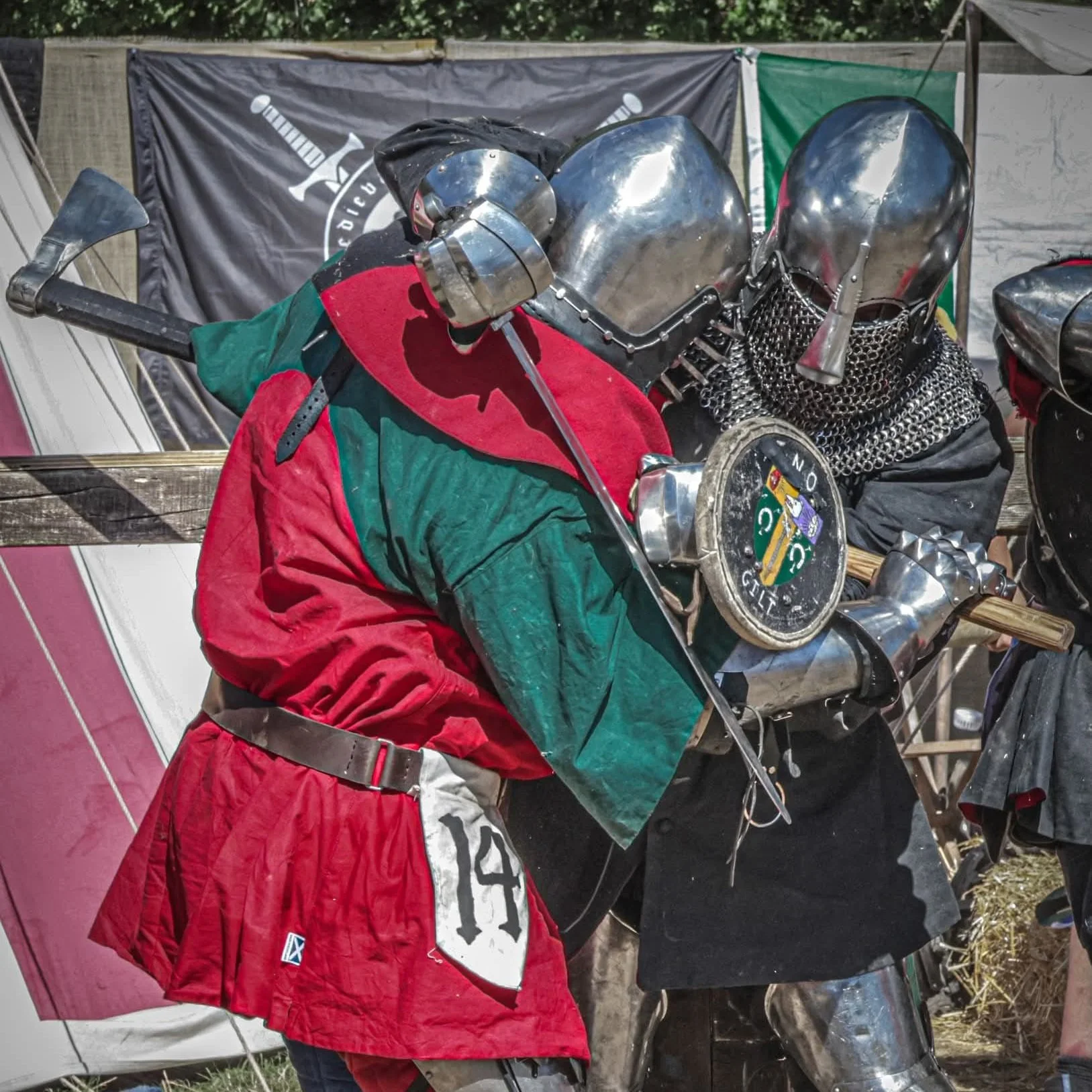 Close-up of two knights in medieval armor, holding a large sword and shield at a reenactment event.