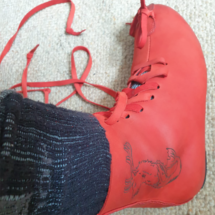 Red dance sneaker with laces untied, worn with navy blue sock on beige carpet.