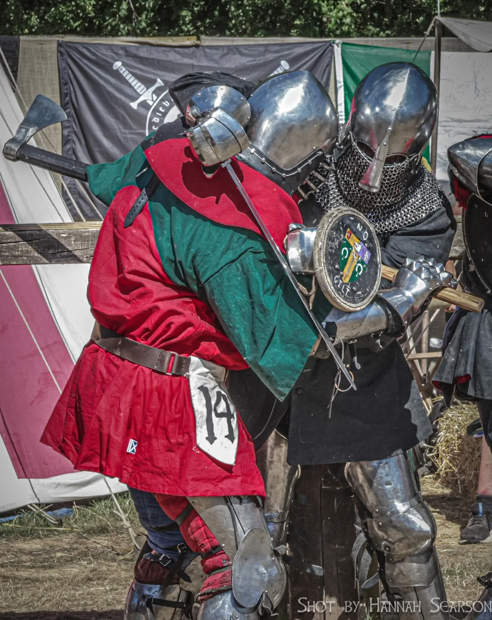 Two individuals dressed in medieval knight costumes, engaging in a sword fight at a festival or reenactment event.
