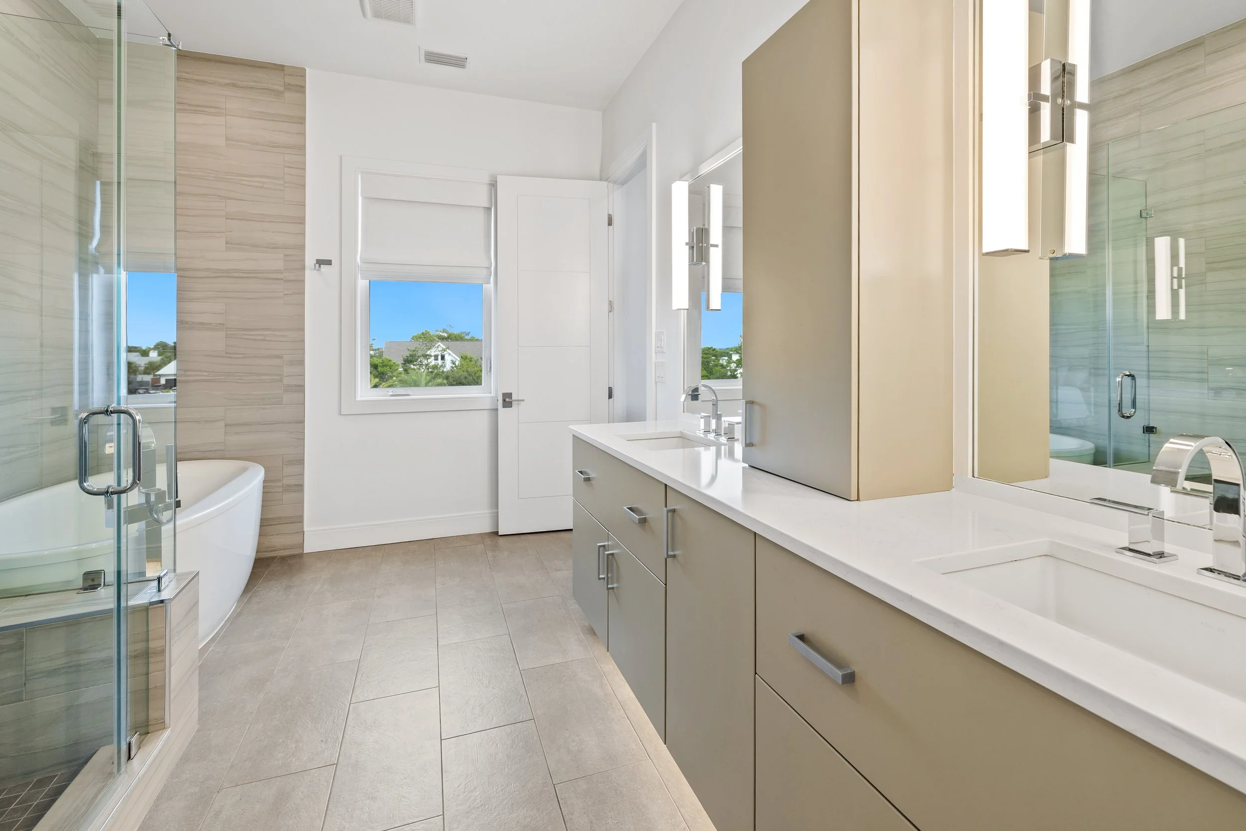 Modern master bathroom with dual sinks, large mirror, built-in cabinetry, a bathtub, and a glass-enclosed shower, with windows with a view of the swimming pool.