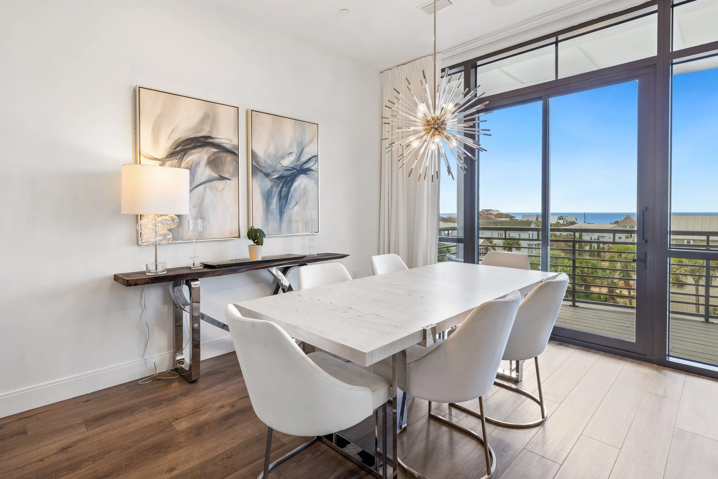 Modern dining room with a white table, six white chairs, a sliding glass door leading to a balcony, and ocean view