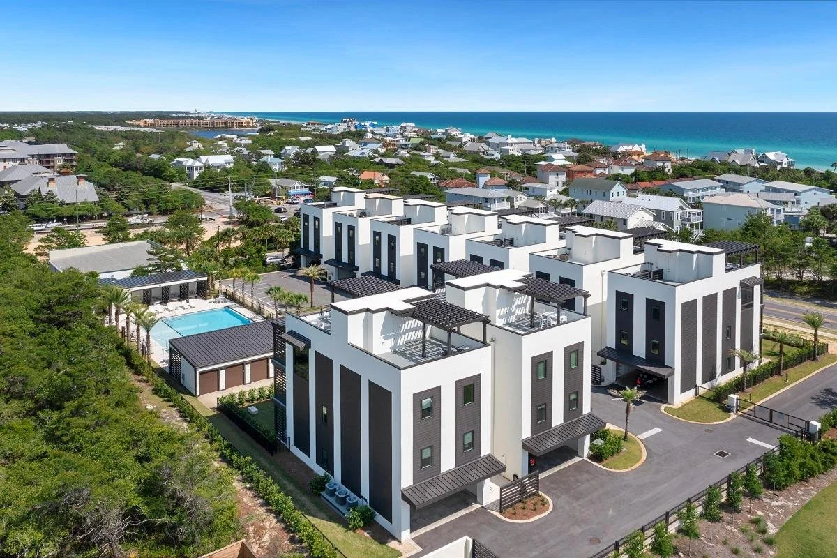 Modern white luxury homes with black accents near the coast, featuring rooftop patios, a pool, and lush greenery.  One block from the beach.