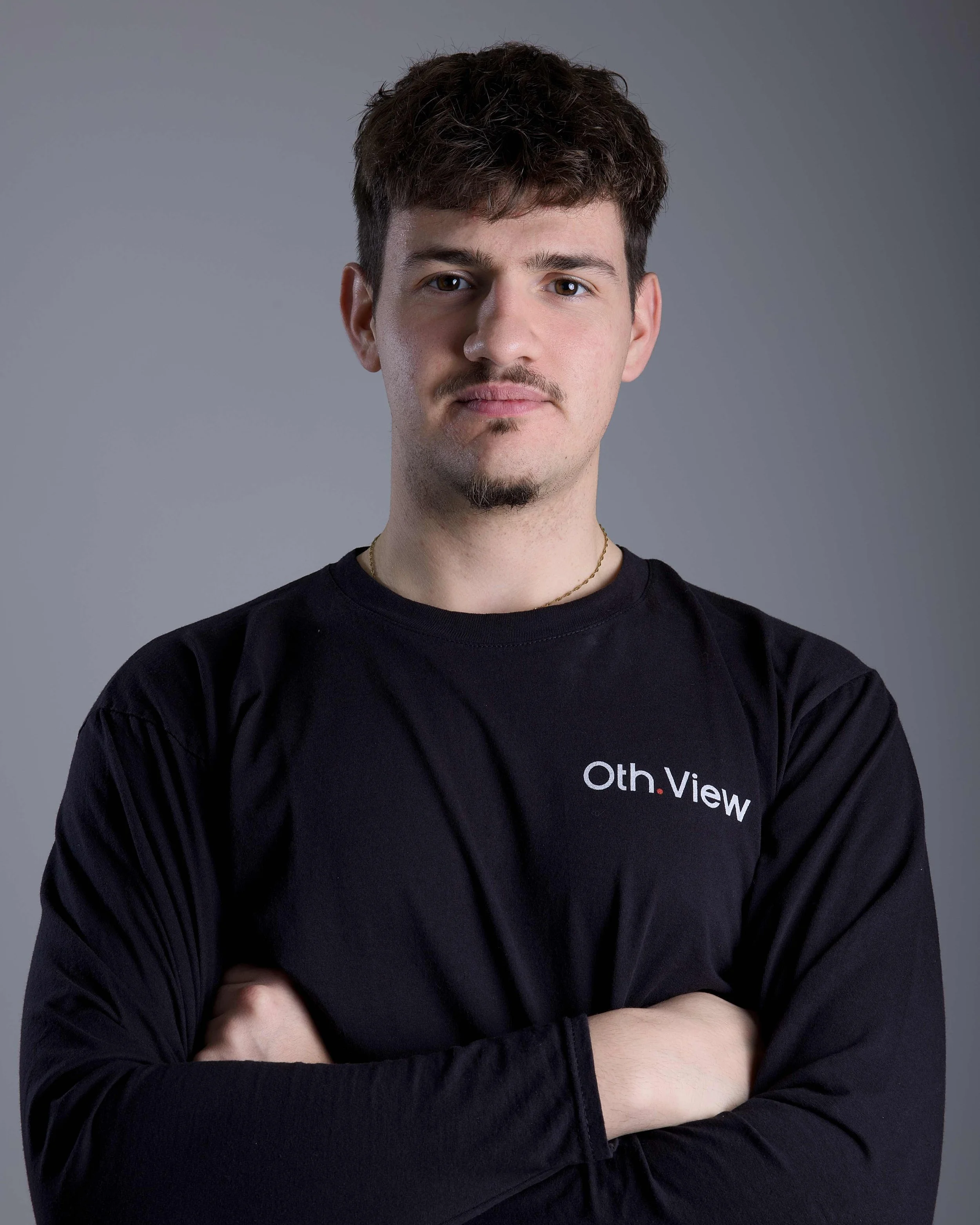 Ein junger Mann mit Locken, Brille und einem weißen Hemd hält eine professionelle Videokamera.