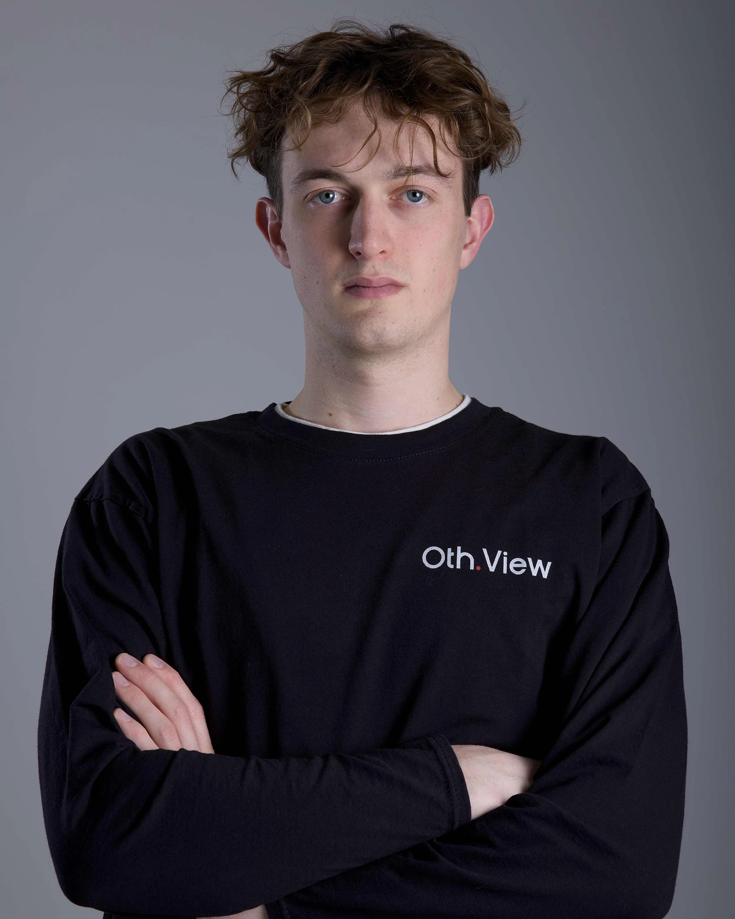 Junger Mann mit braunen kurzen Haaren, schwarzem T-Shirt, blickt nach links, im Hintergrund mehrfarbiger Lichtstrahl auf grauem Hintergrund