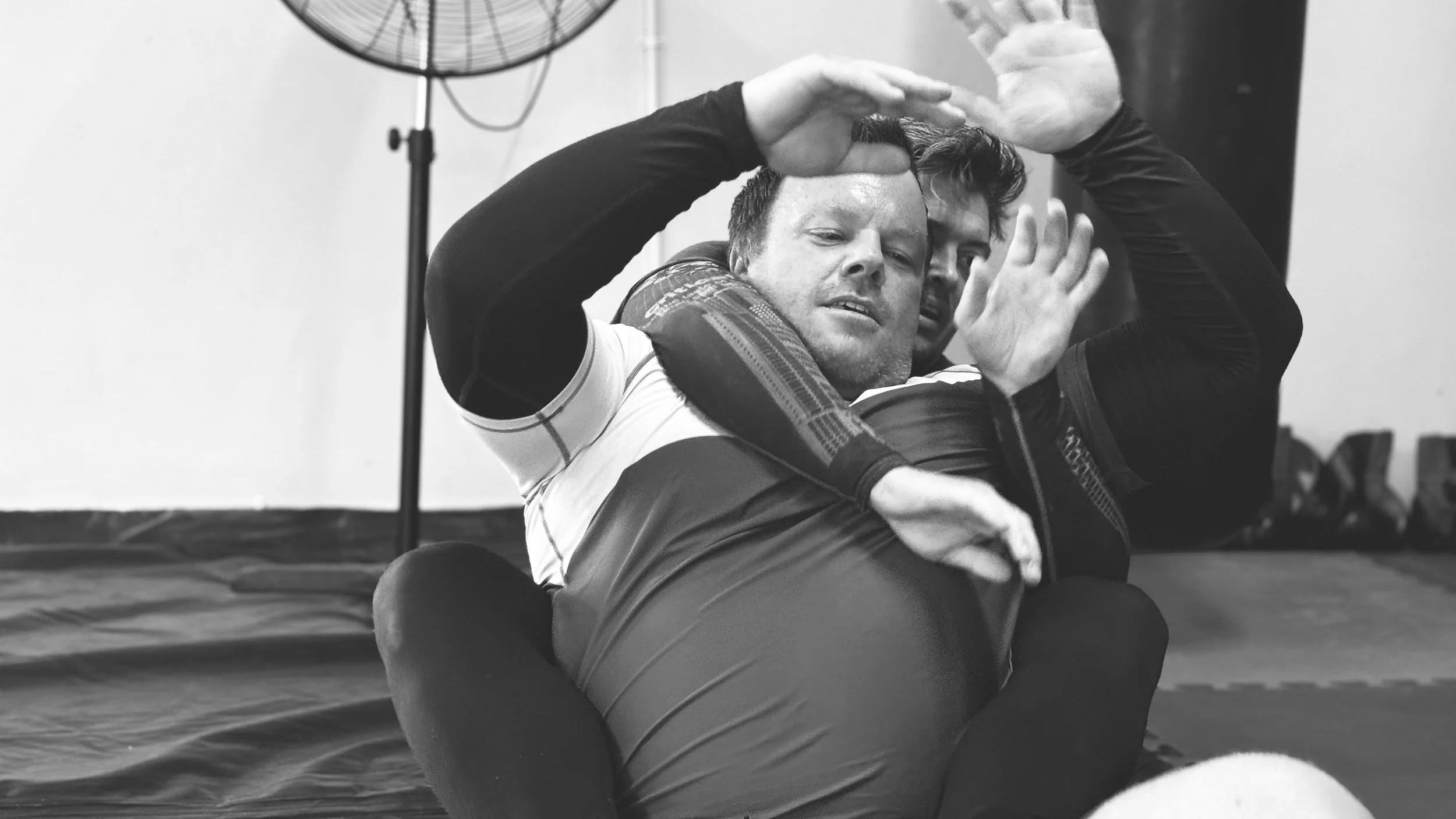 Two men practicing Brazilian Jiu-Jitsu, with one man pinning the other to the ground, in a gym setting.