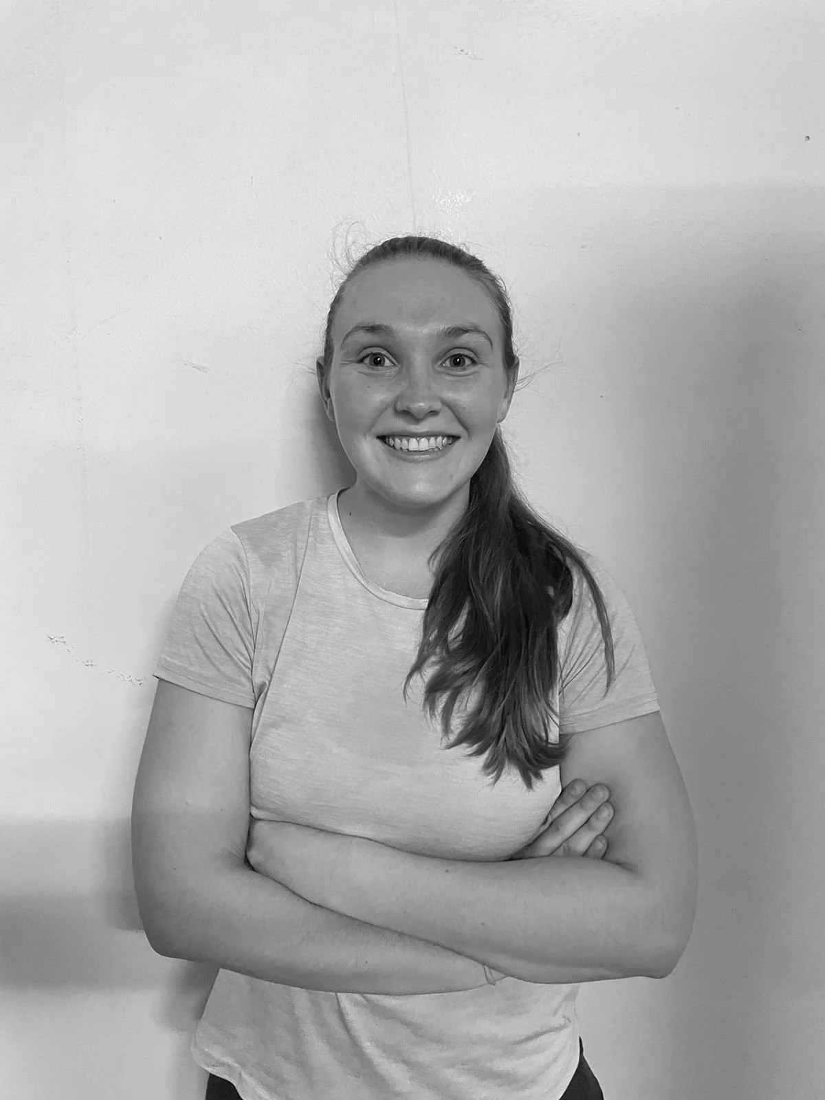 Black and white photo of a smiling woman with arms crossed, standing against a plain wall.