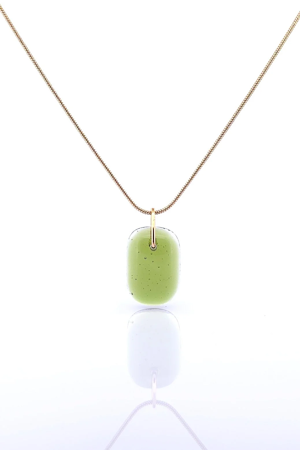 A dark green glass pendant on a gold chain against a white reflective background..