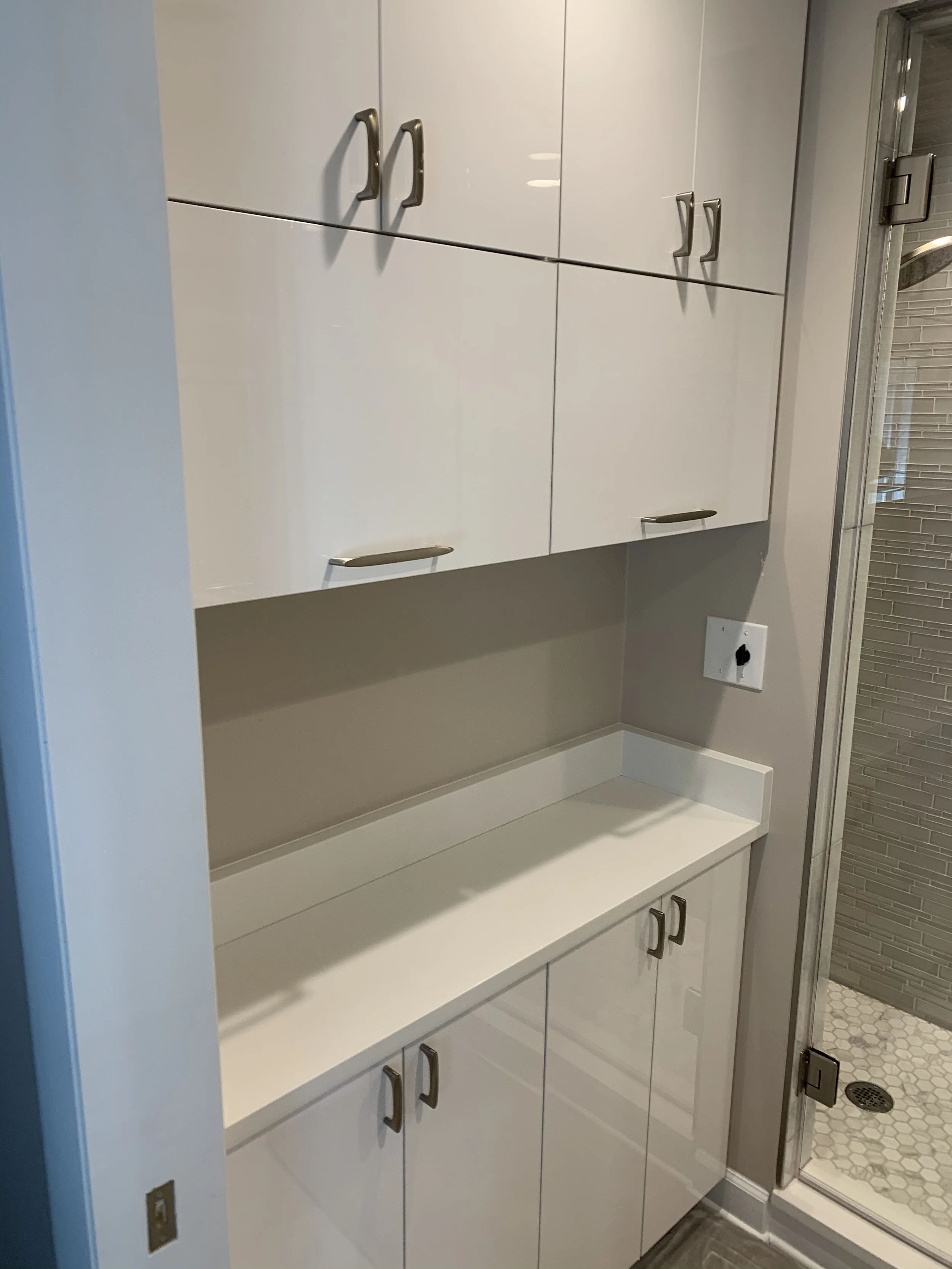 White kitchen cabinets and countertops near a bathroom shower with gray hexagonal tiles.