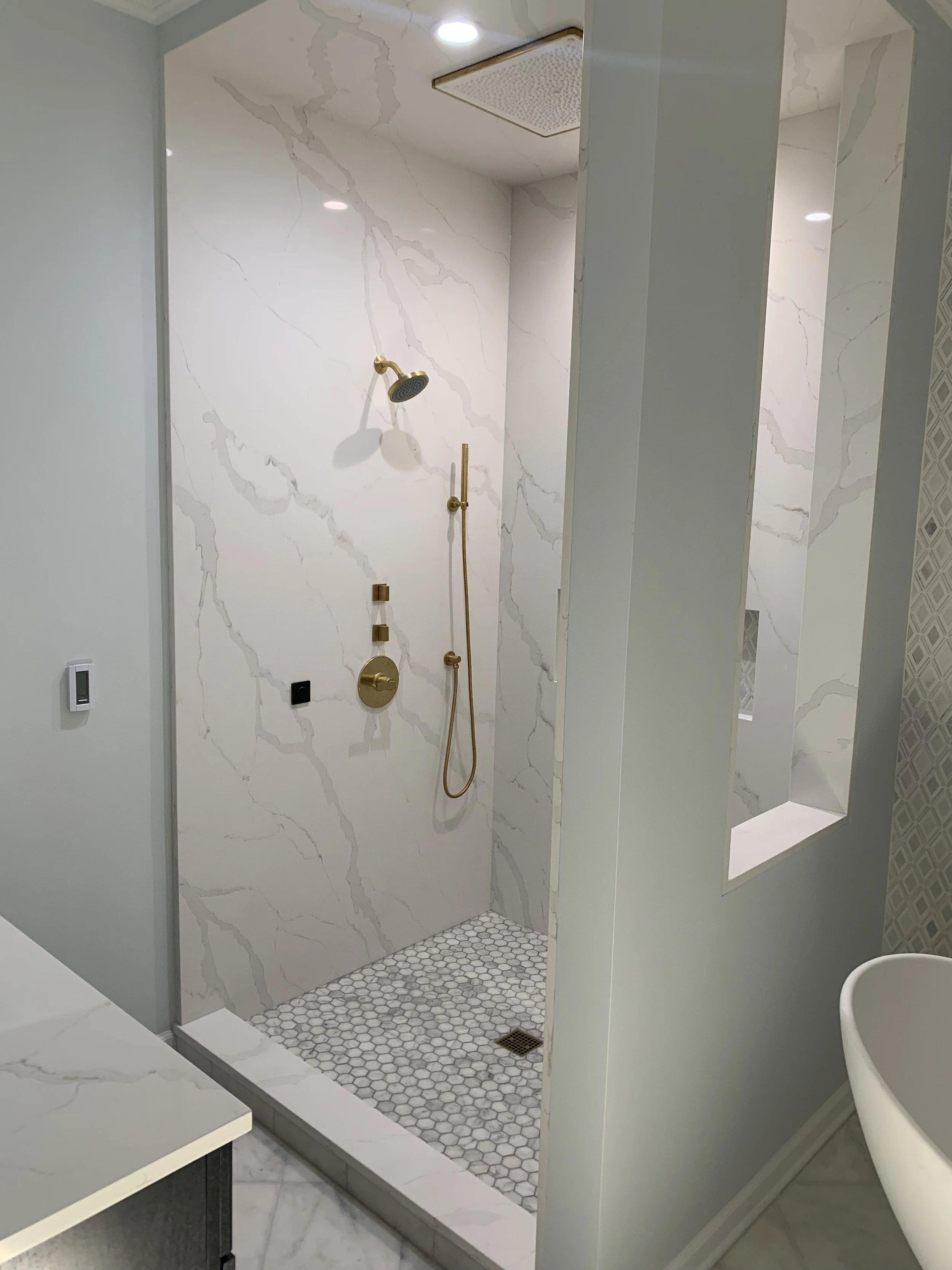 Modern walk-in shower with white marble walls, gold fixtures, and hexagonal tile floor.