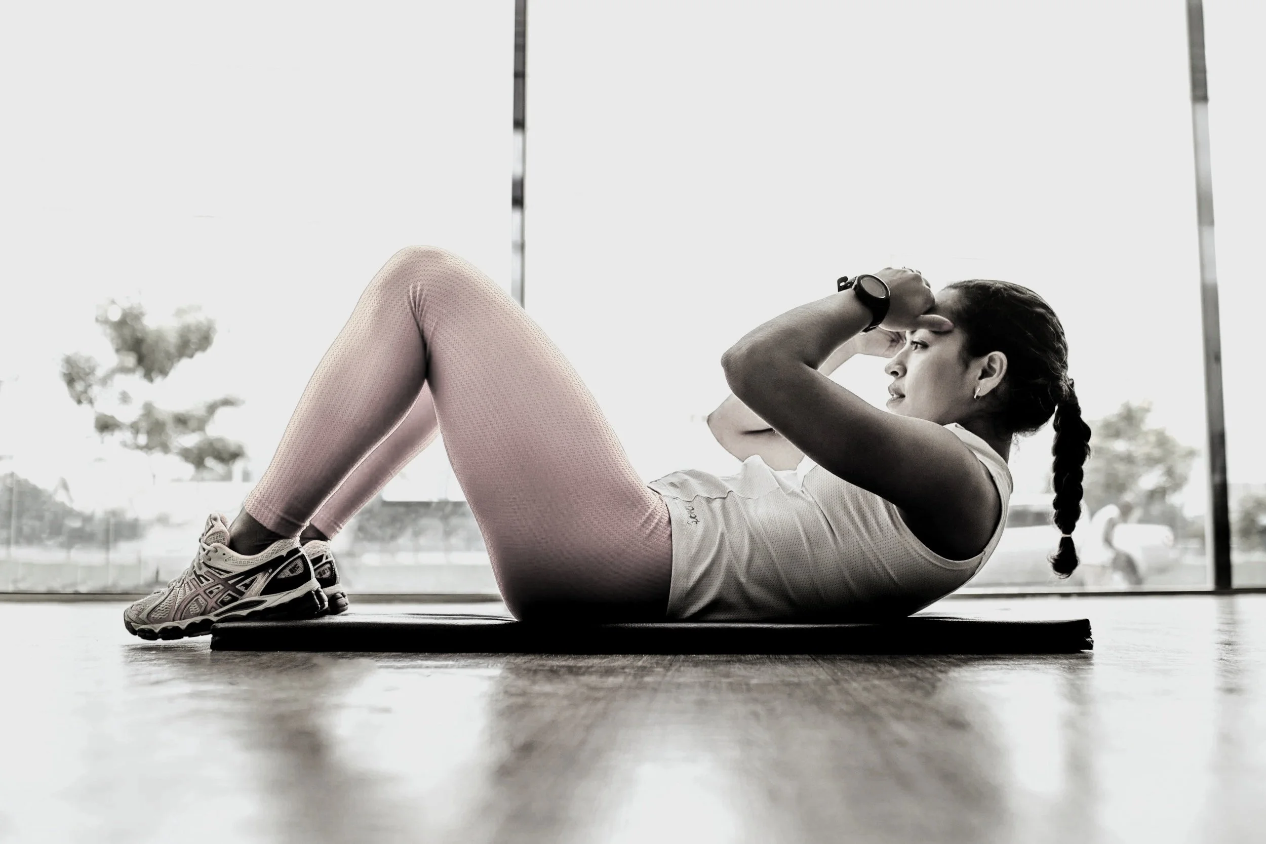 Woman performing sit-up exercise on yoga mat in gym, black and white photo.