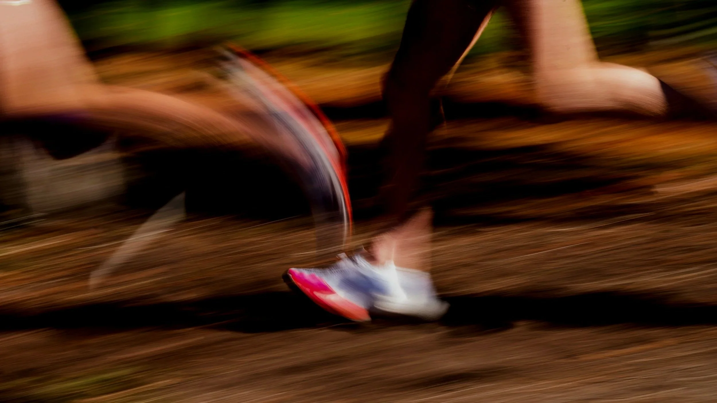 Close-up of a runner's legs and feet moving at high speed on a dirt trail, with motion blur.