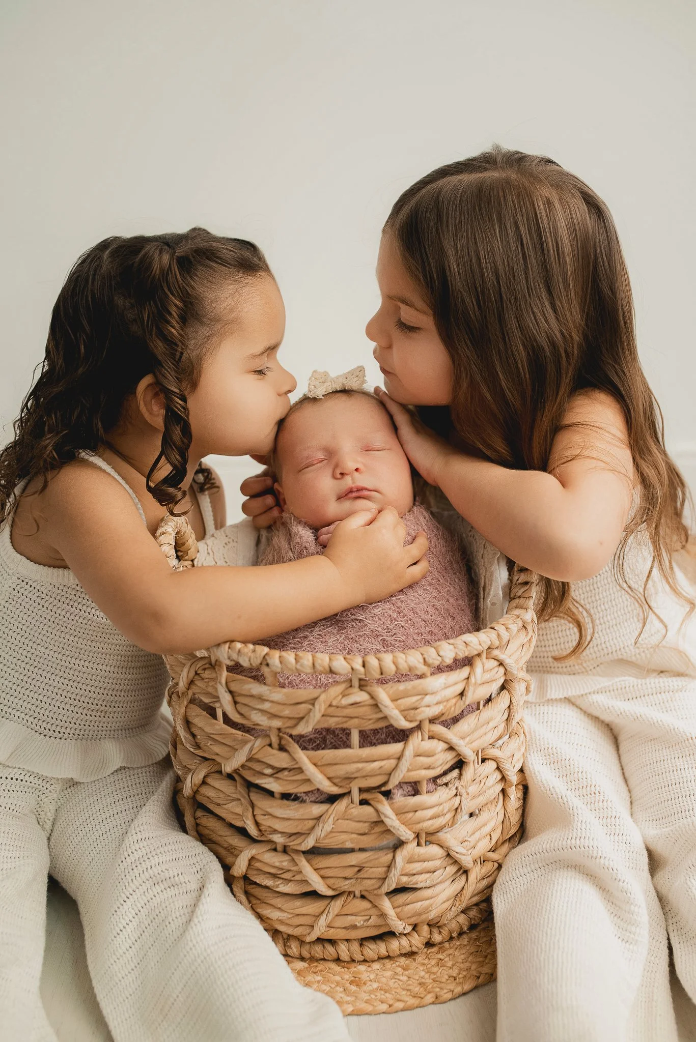Two older sisters with their sleeping newborn sibling during a sibling newborn photography session.