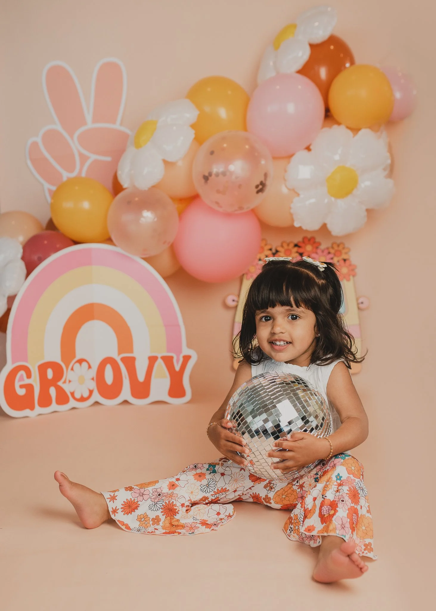 Young girl smiling in a colorful groovy themed setup during a children’s portrait photography session.