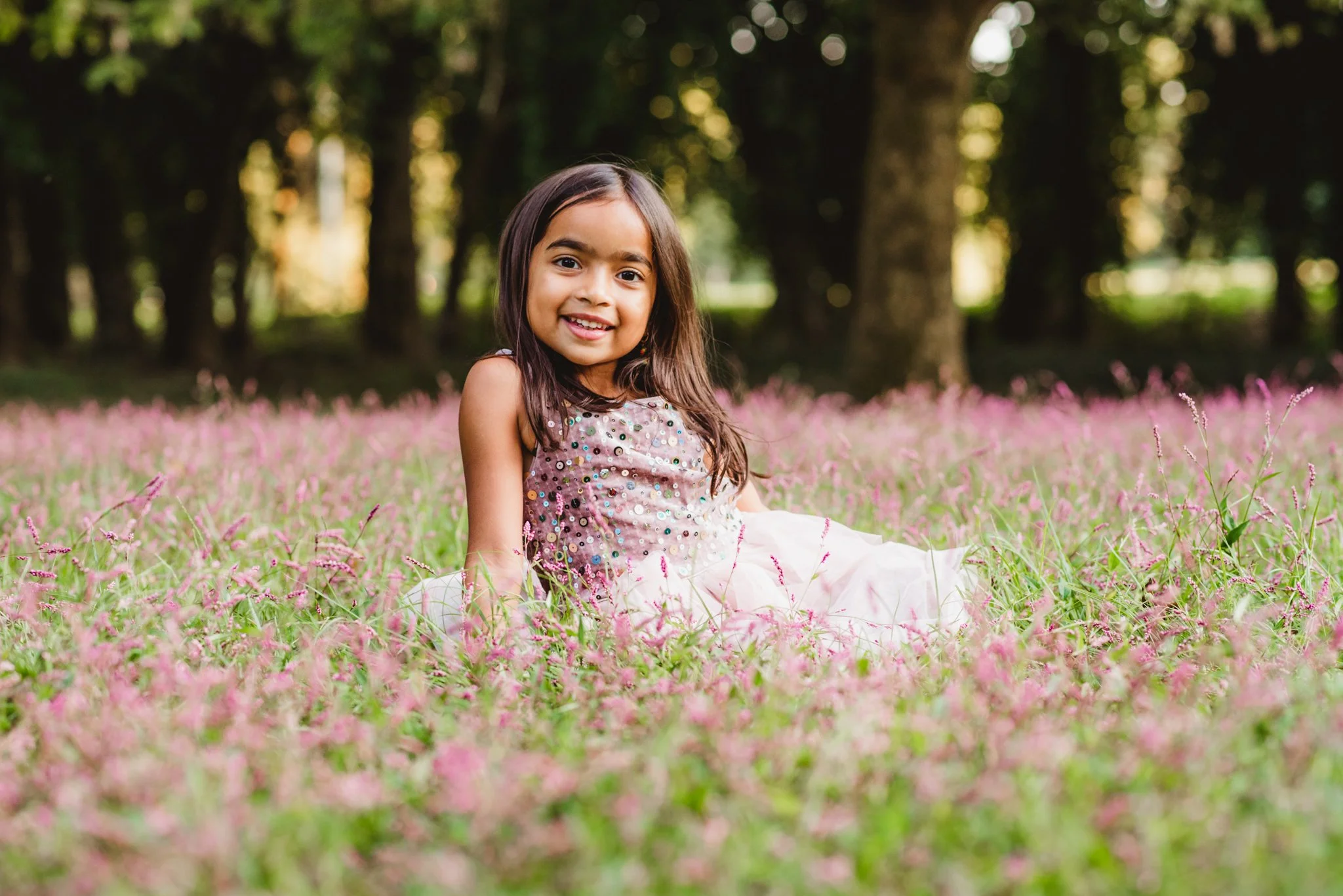 Young girl smiling in a field of pink flowers during an outdoor children’s portrait session.
