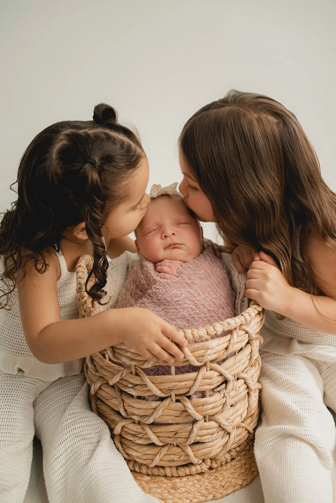 Two sisters kissing their newborn sibling during a newborn photography session.