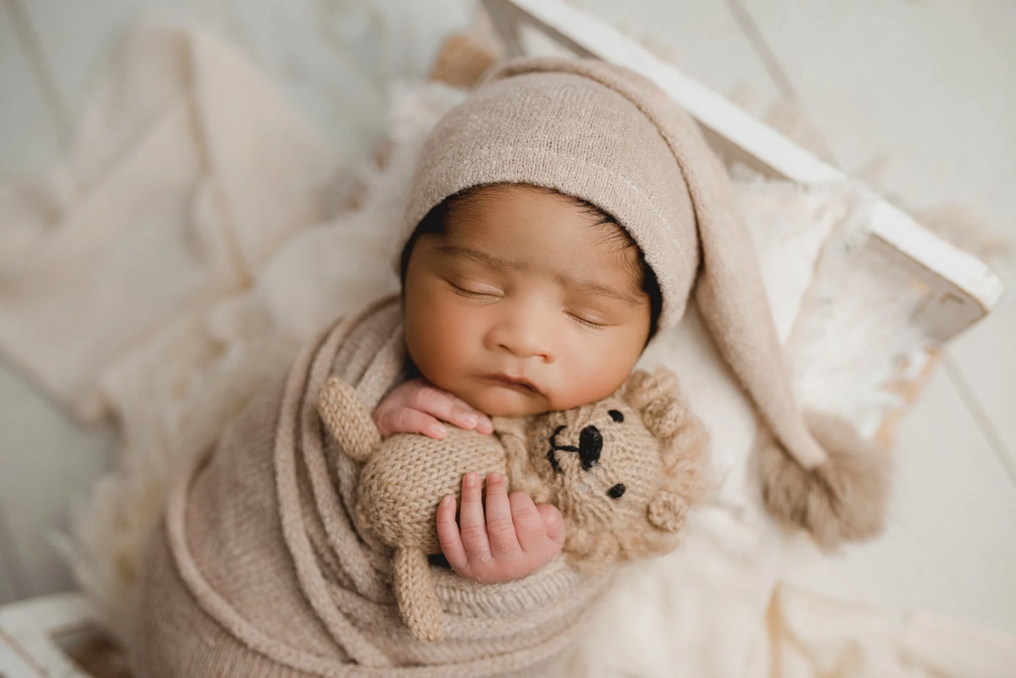 Sleeping newborn baby in neutral tones holding a small teddy bear during a posed newborn photography session.