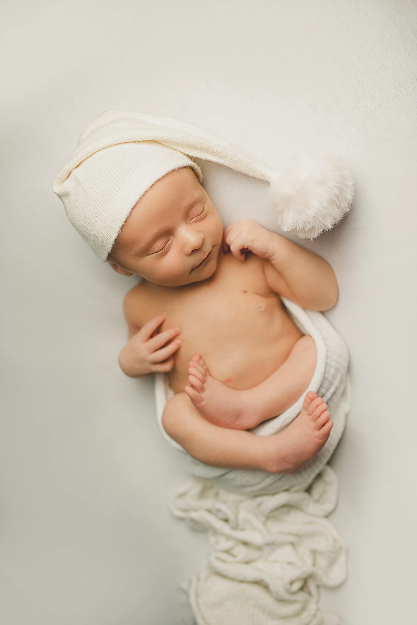 Sleeping newborn baby in a white knit bonnet during a posed newborn photography session.